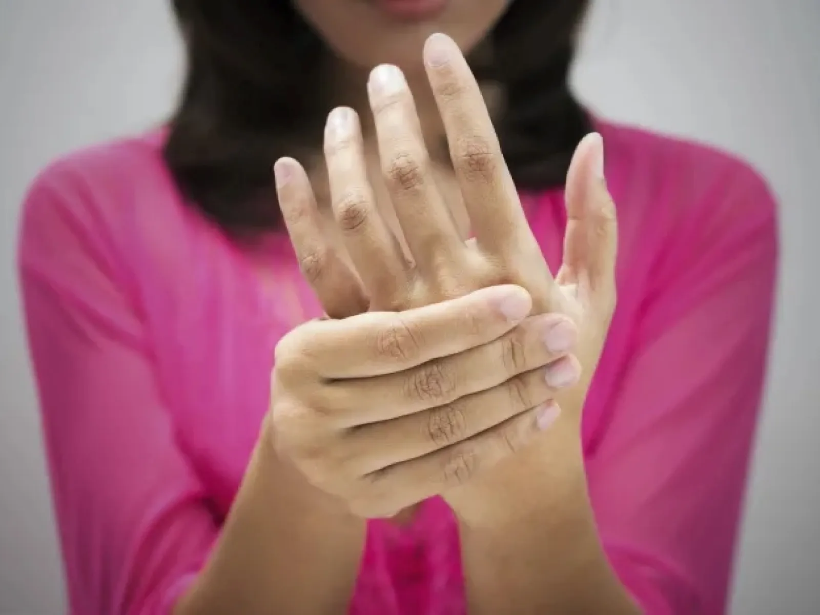 Person in pink shirt holding and rubbing their painful wrist with their other hand