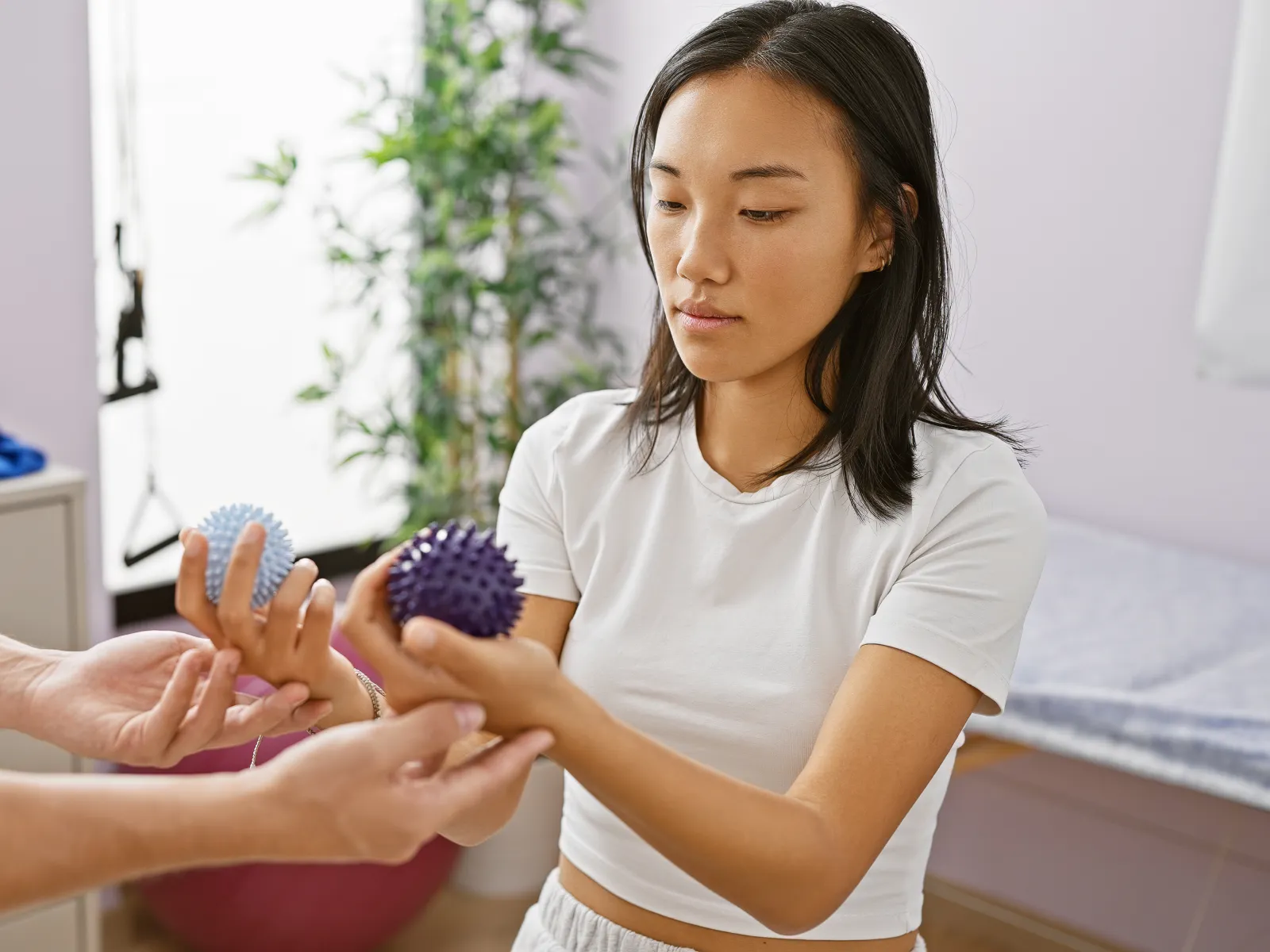 Therapist guides young woman in hand rehabilitation exercises using spiky therapy balls in clinical setting