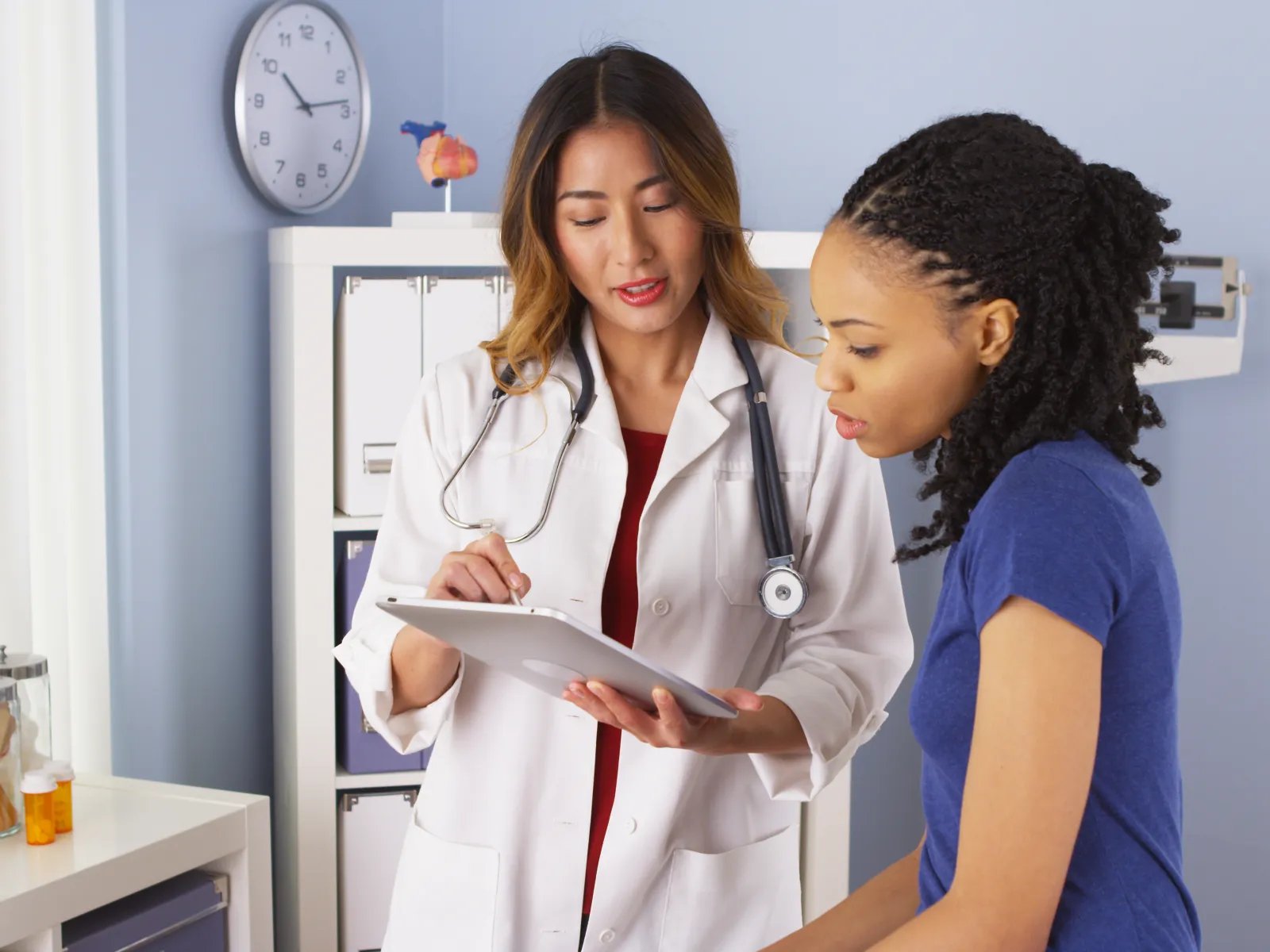 Doctor explaining medical information on a tablet to a female patient in a clinic room.
