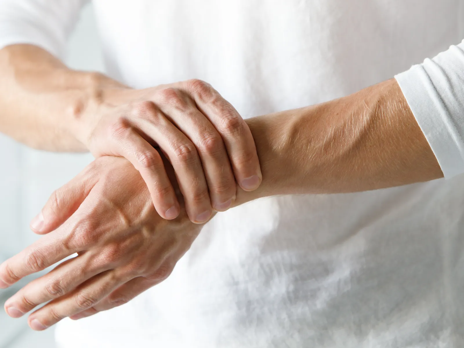 Close-up of a person rubbing their wrist showing joint pain or discomfort against a white shirt background