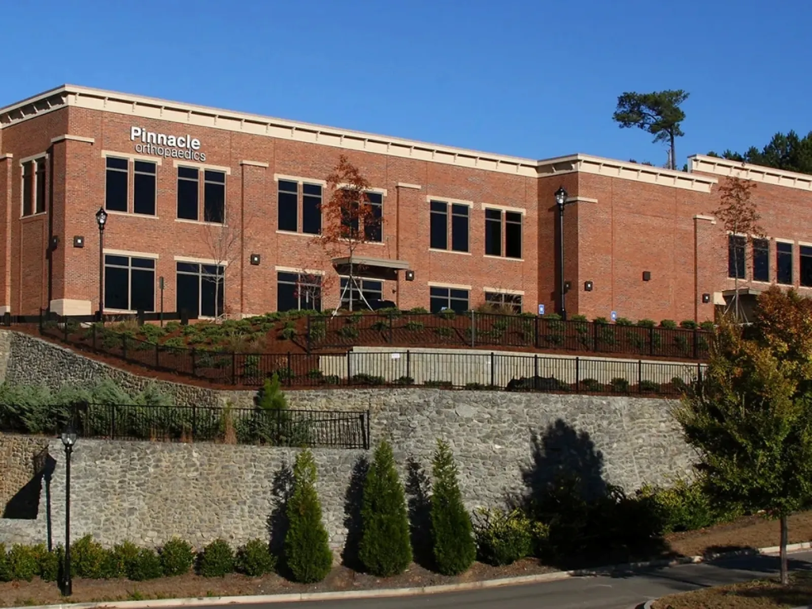 Modern two-story brick building of Pinnacle Orthopaedics under a clear blue sky with landscaping and stone retaining wall.