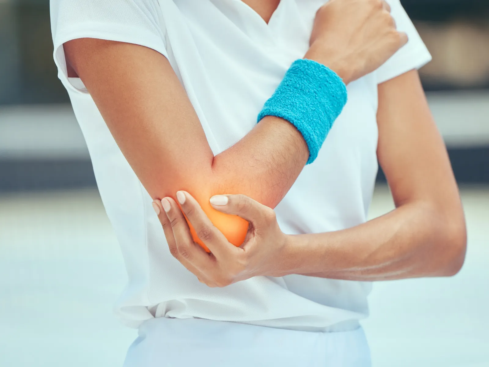 Person in white sportswear holding painful elbow with a blue sweatband, indicating elbow pain or injury.