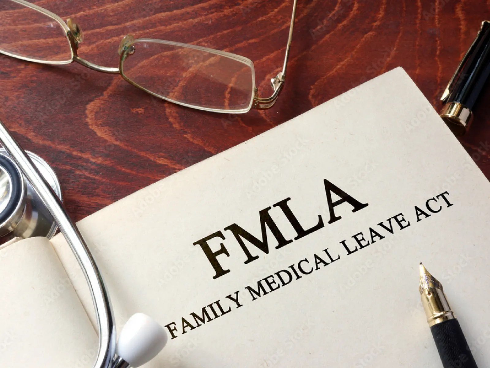 Open book titled FMLA Family Medical Leave Act with stethoscope, glasses, and pen on wooden table.