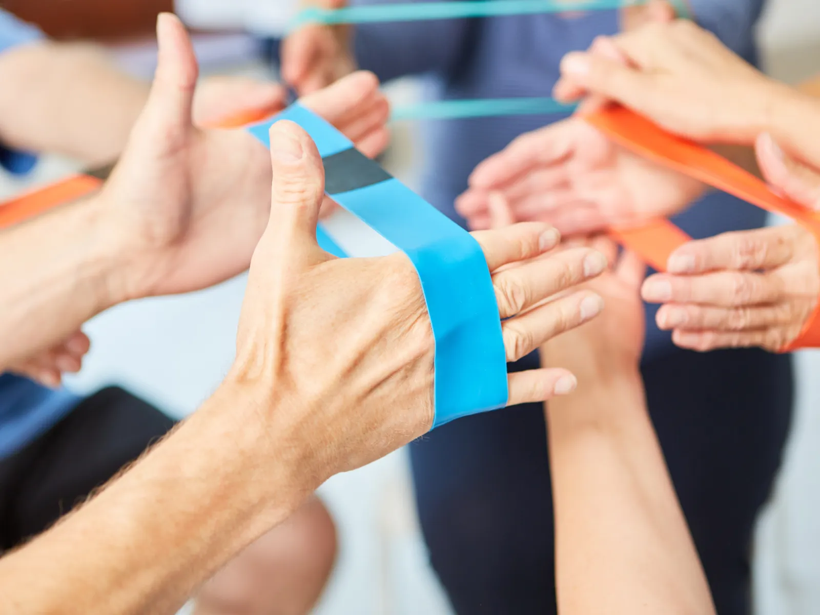 Close-up of hands using colorful resistance bands for physical therapy or exercise in a group setting.