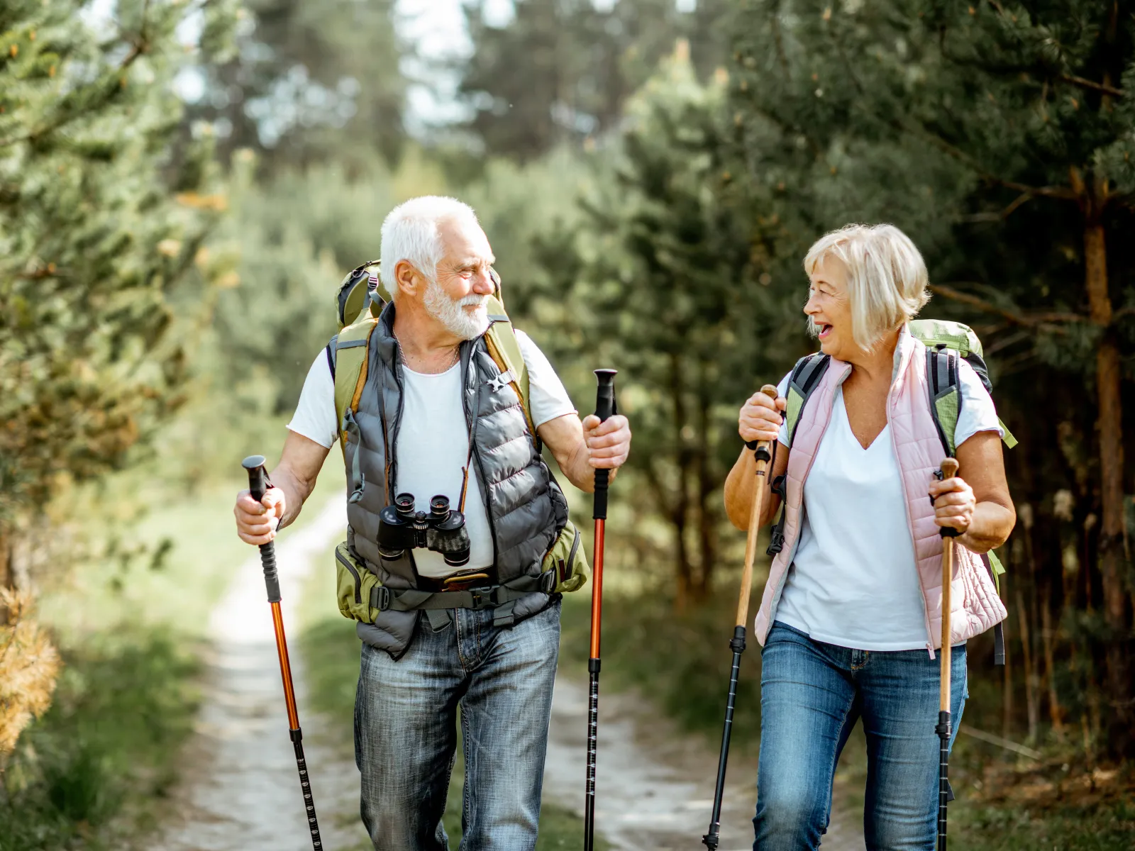 Senior couple hiking with backpacks and walking poles on a forest trail, enjoying nature and each other's company.