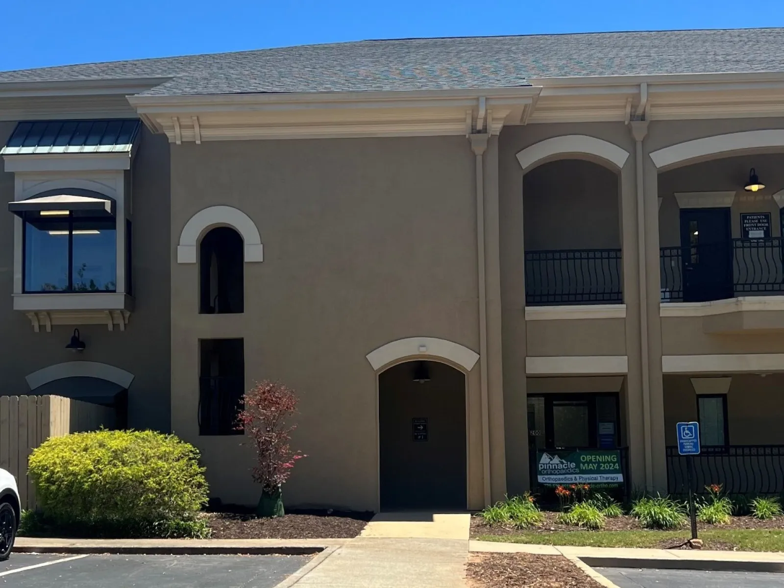 Modern two-story office building with arched doorways, white trim, and landscaping under a clear blue sky.