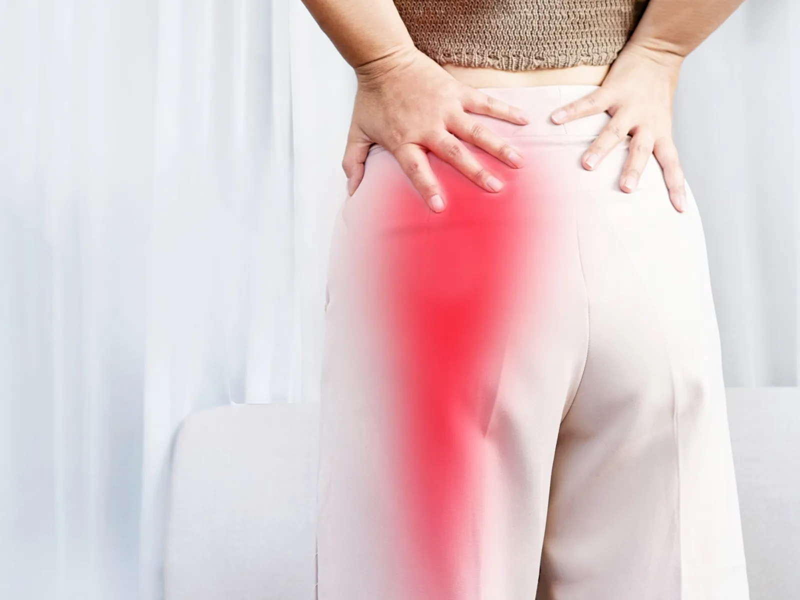 Person holding lower back and hip with red area indicating pain or discomfort in the hip region.