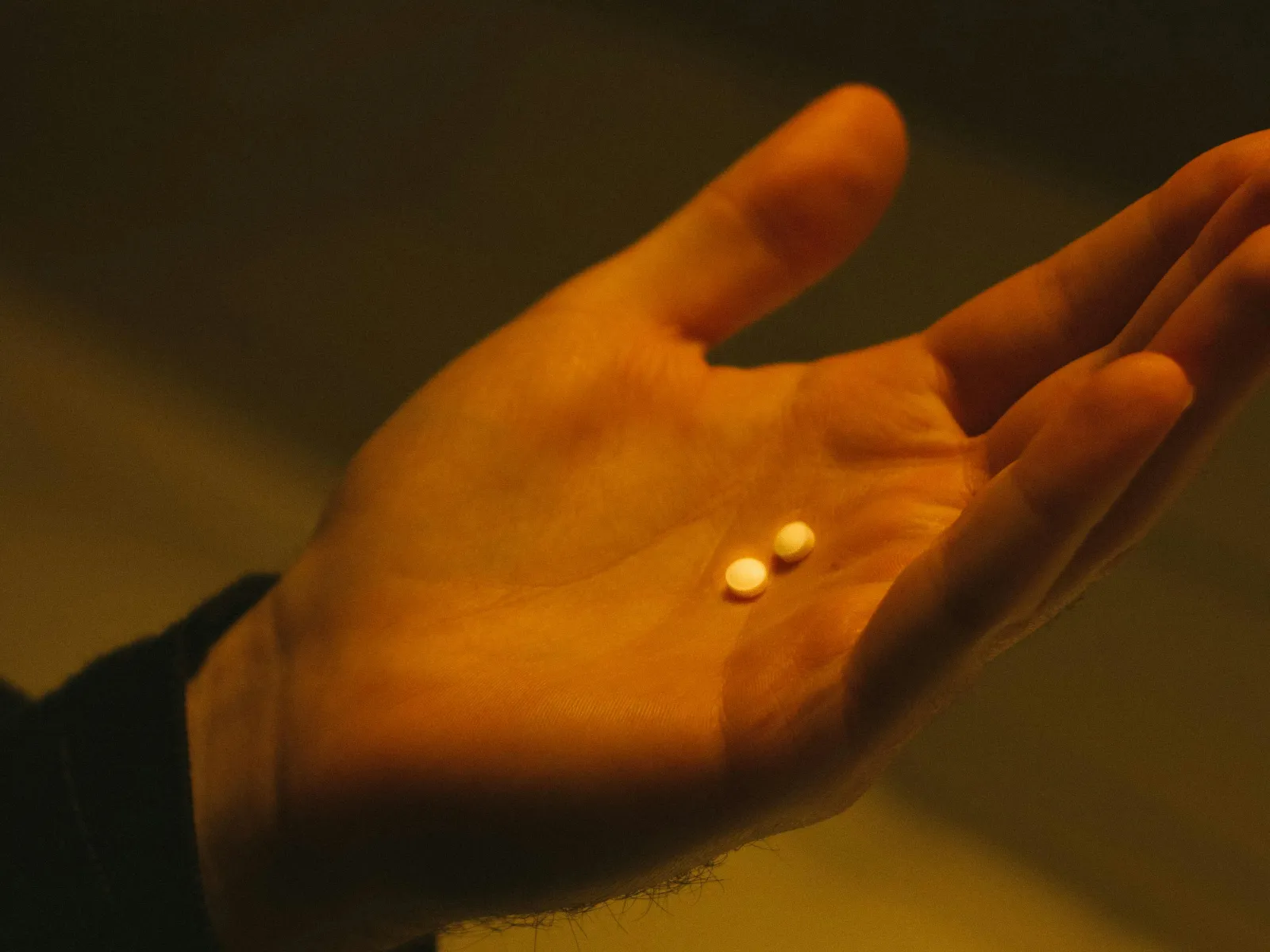 Close-up of a hand holding two small white pills under warm lighting.