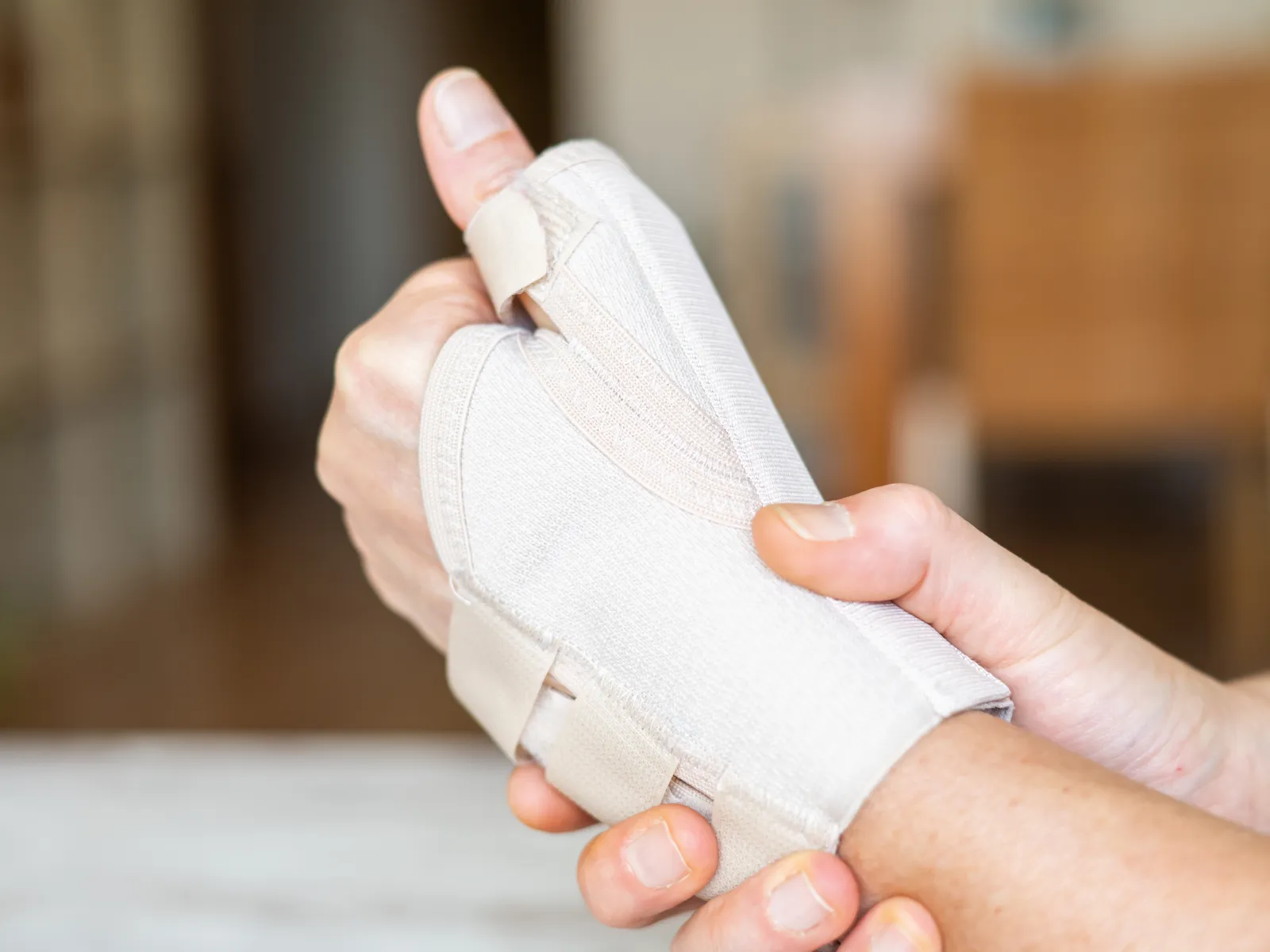 Person wearing beige wrist and thumb brace for support and injury recovery on a blurred background.