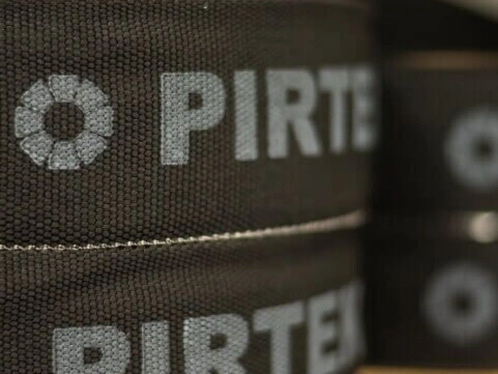 Close-up of black fabric rolls with the white Pirtek logo stacked on a shelf.
