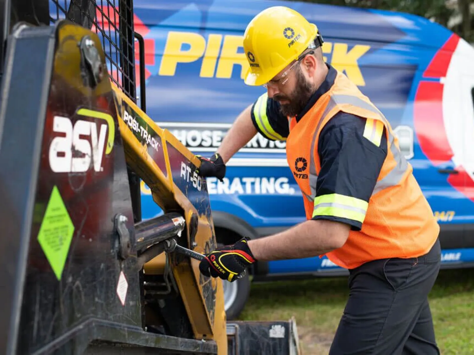 Construction worker in safety gear operating ASV Posi-Track RT-50 equipment near a service van outdoors.