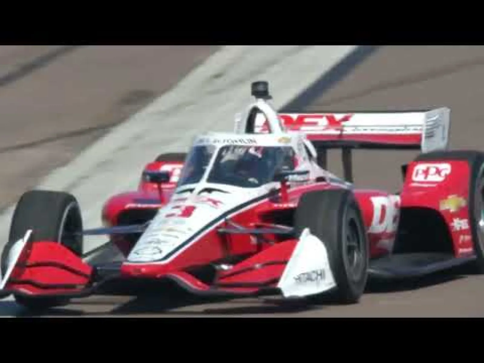 IndyCar racing car speeding on track with red, white, and black colors and visible sponsor logos.