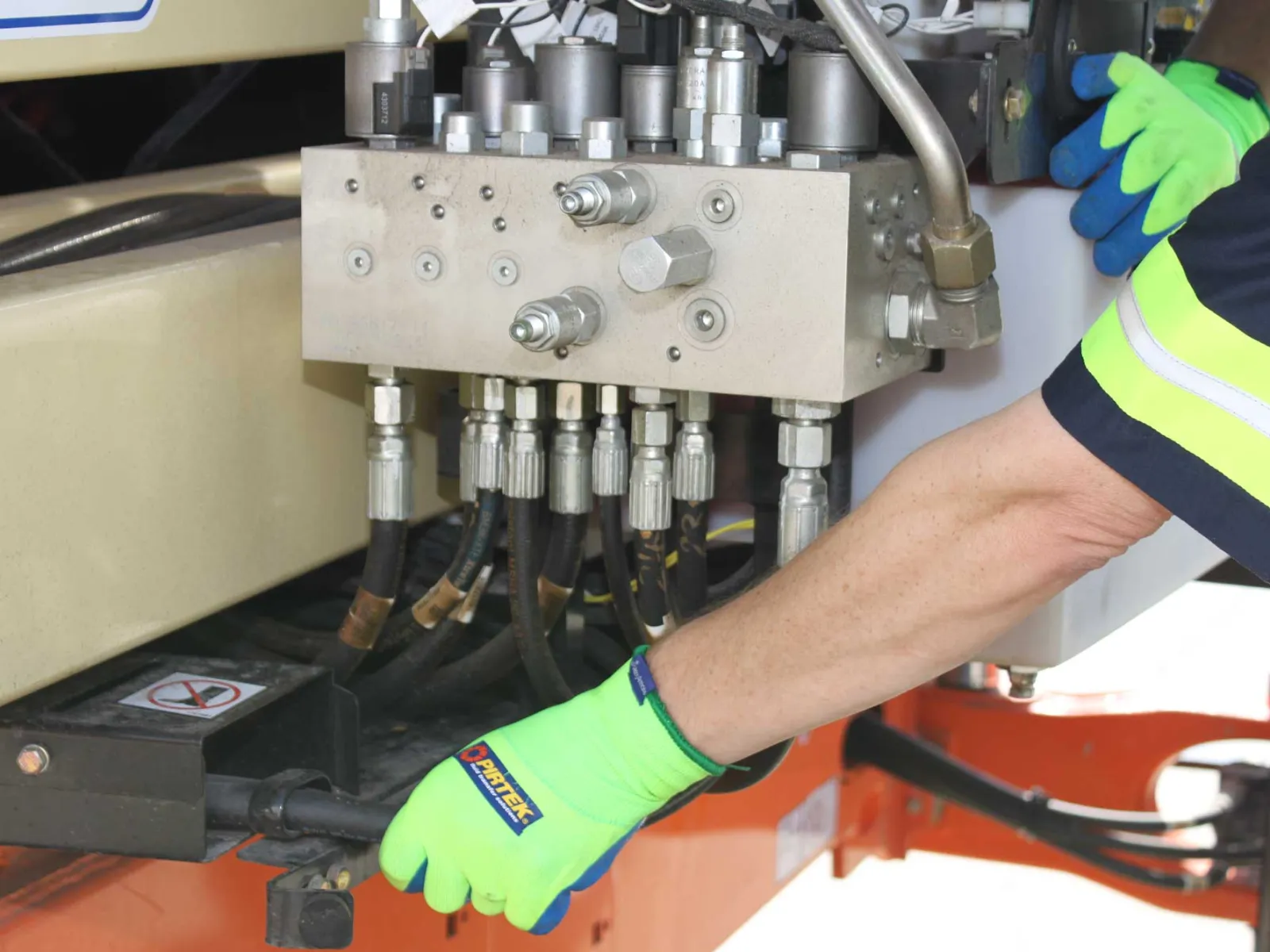 Worker wearing bright green safety gloves operating hydraulic machinery with metal pipes and connectors.