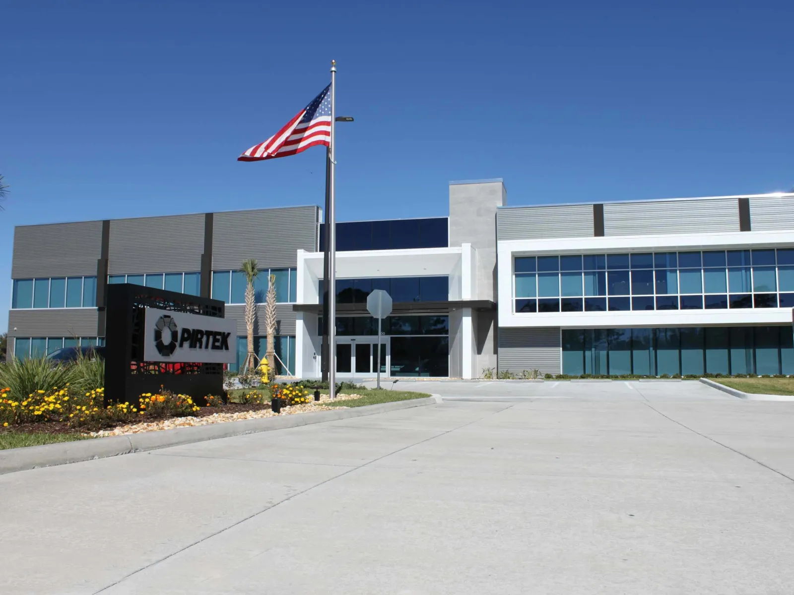 Modern two-story office building with large windows, American flag, and PRITEX company sign in front.