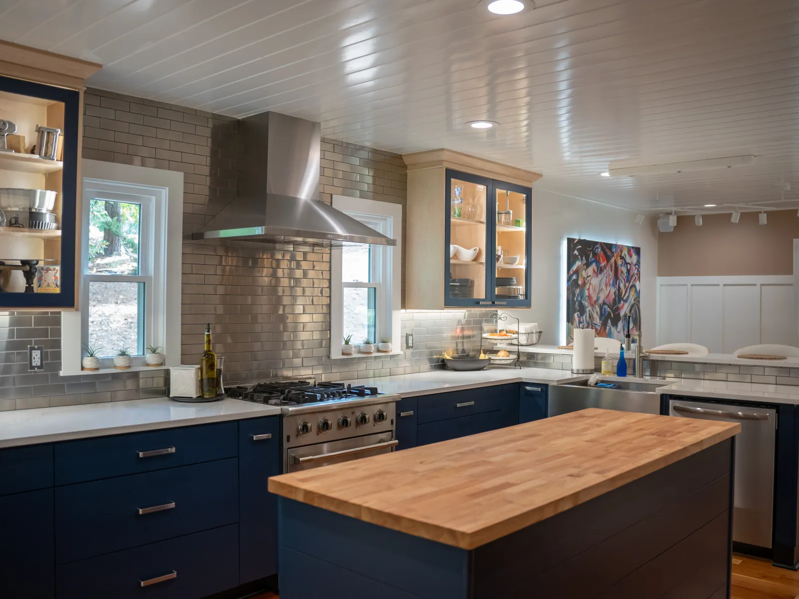Modern kitchen with blue cabinets, wooden island, stainless steel appliances, and white subway tile backsplash.