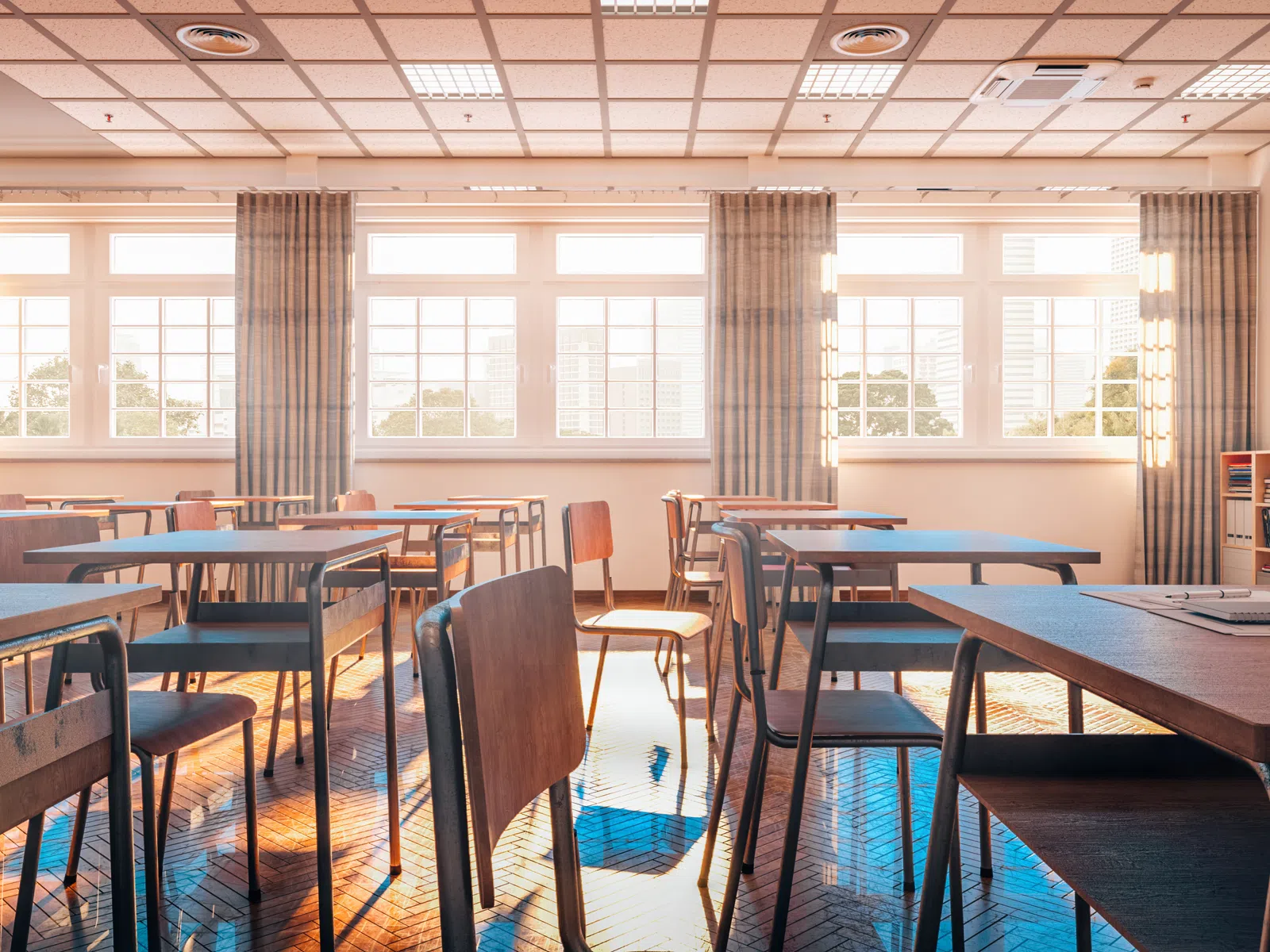Sunlit empty classroom with wooden desks, chairs, large windows, and a chalkboard on the wall.