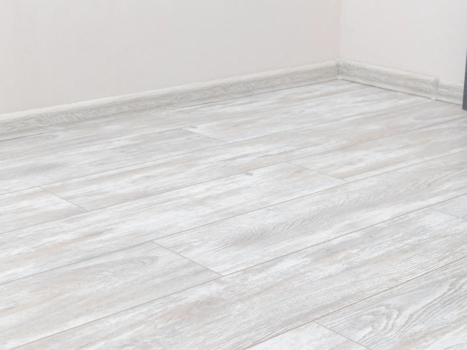 Light gray wood texture laminate flooring installed in a room corner with white walls.