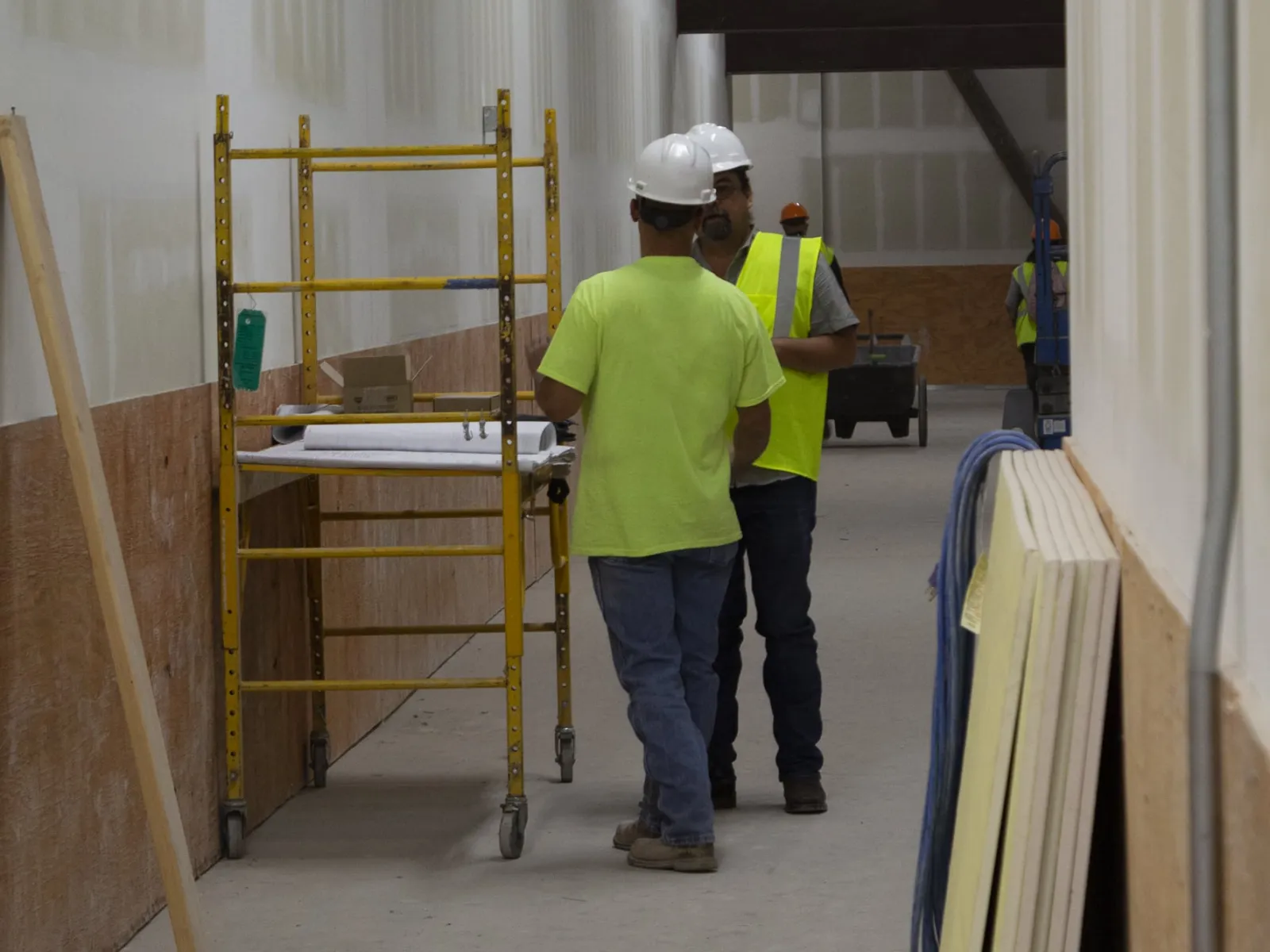 Construction workers wearing safety gear discuss plans next to scaffolding inside a building under renovation.