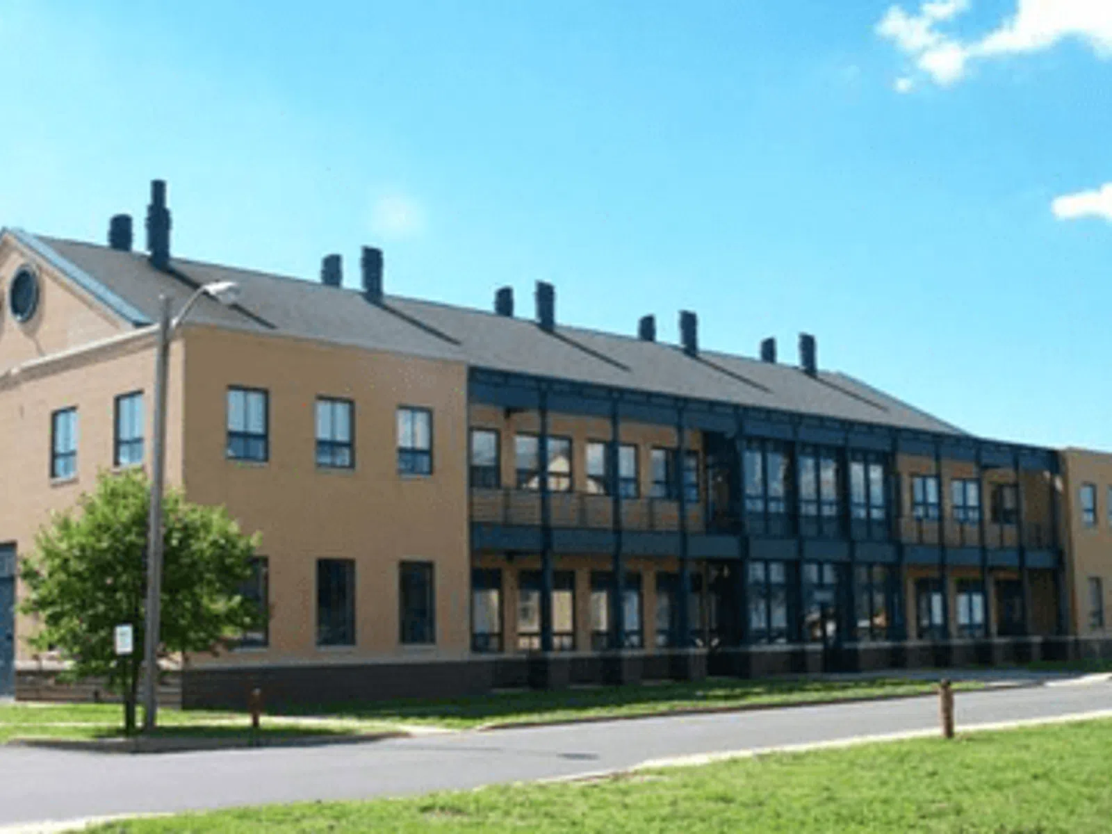 Two-story modern beige building with black window frames and chimneys under a blue sky with clouds.