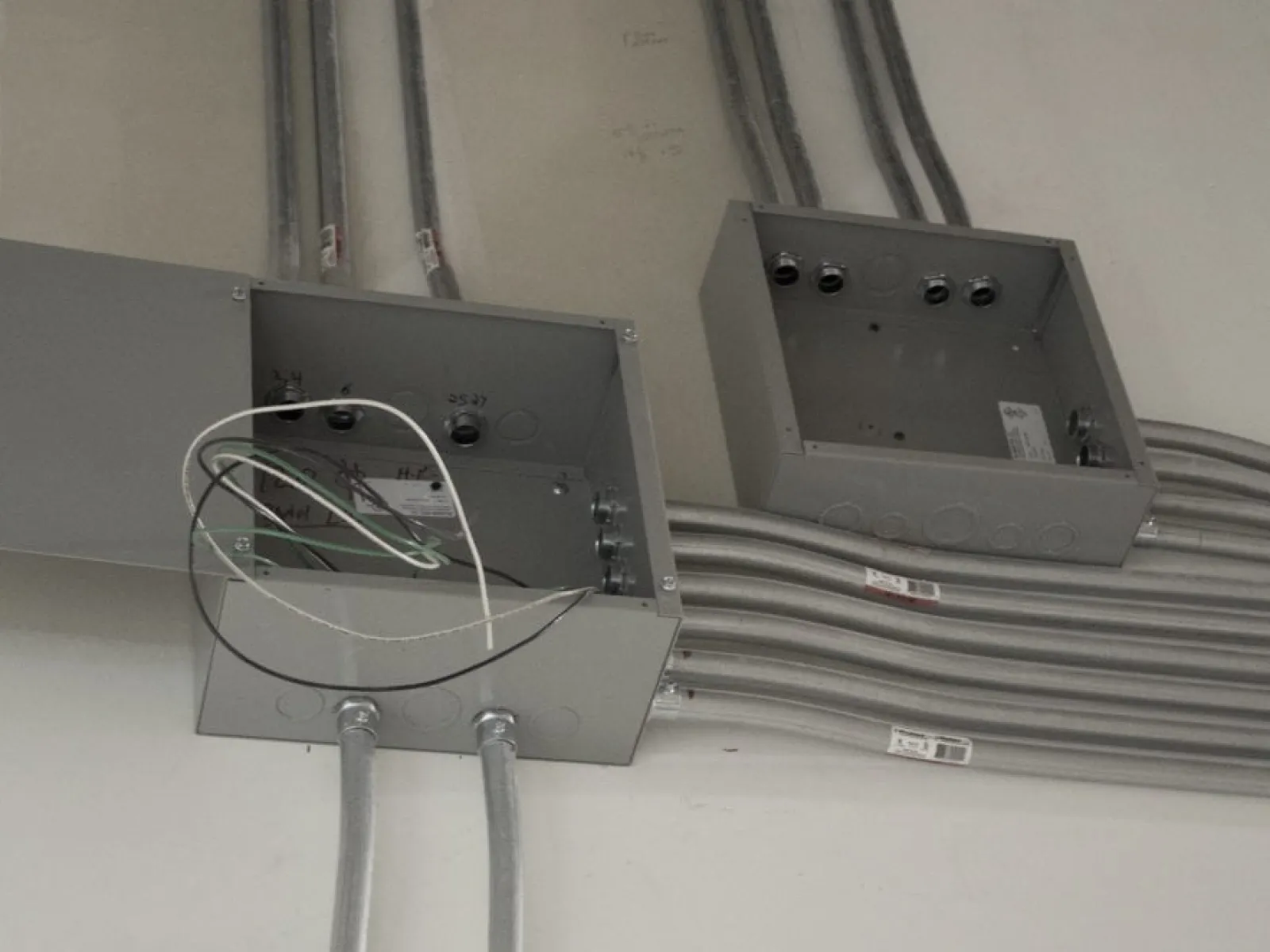 Open electrical junction boxes with metal conduit and wiring installed on a wall during construction.