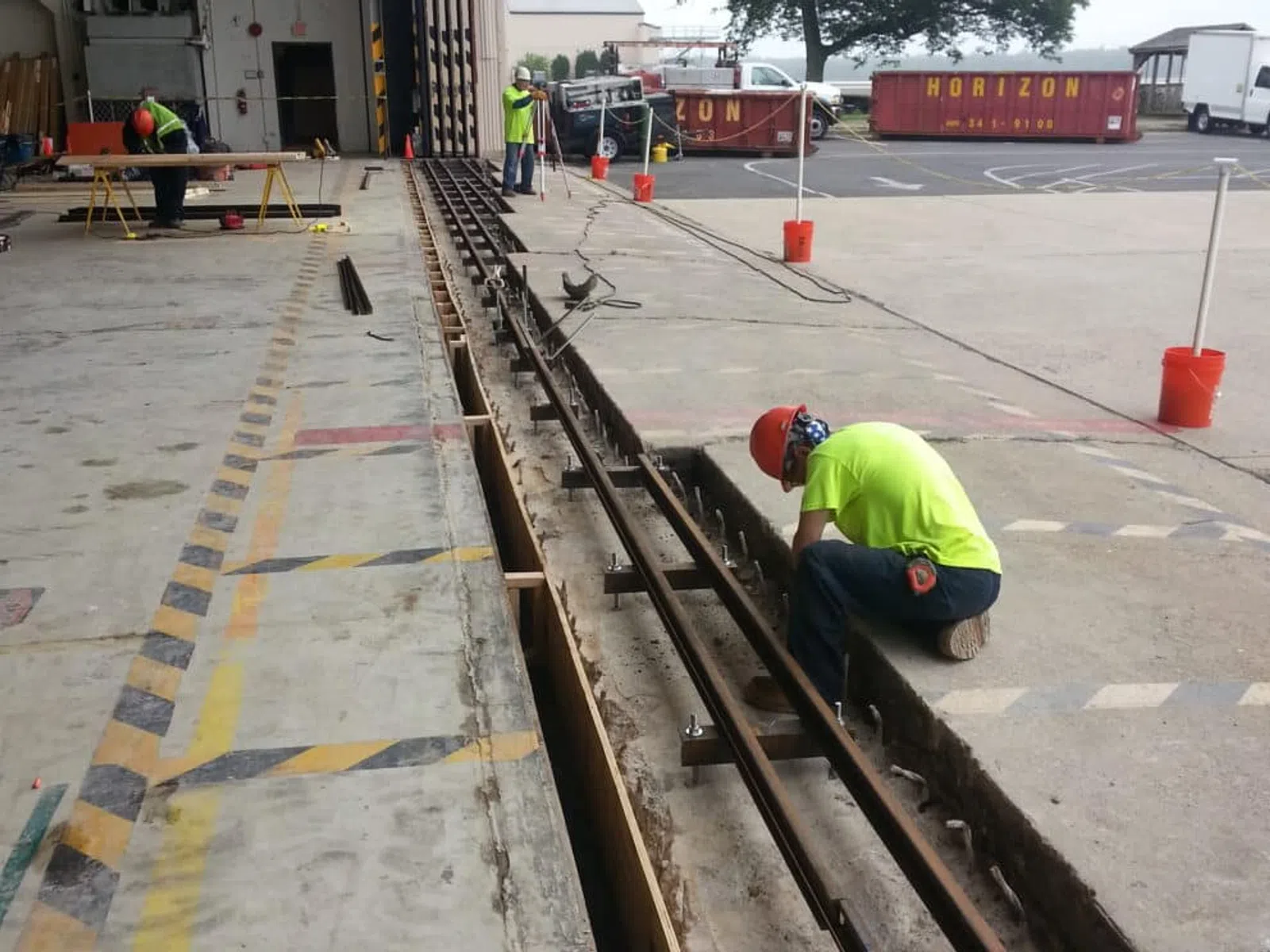Workers in safety gear installing metal rails in a warehouse loading dock area with construction materials nearby.