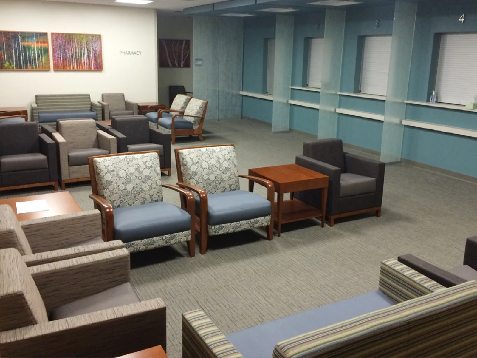 Spacious hospital waiting room with various upholstered chairs, tables, and a pharmacy sign on the wall