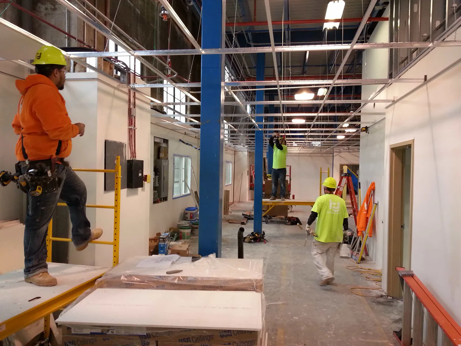 Construction workers install ceiling framework inside a large industrial building under renovation.