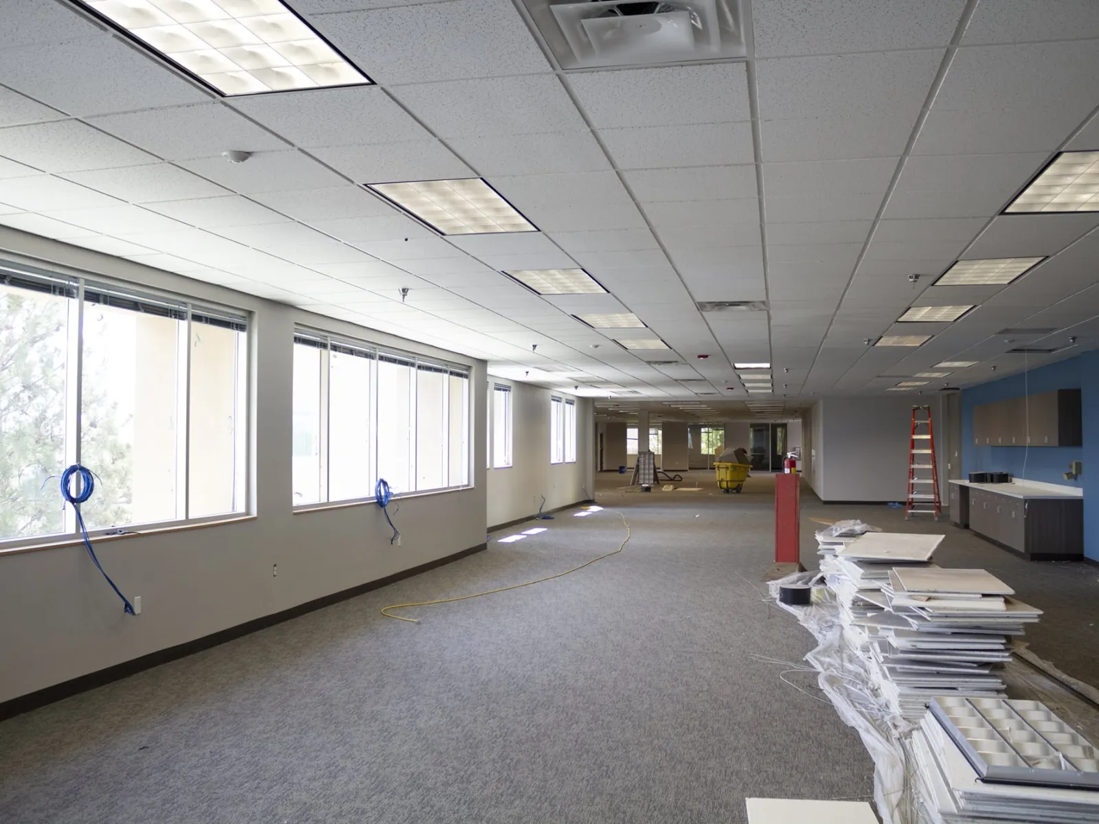 Spacious office interior under renovation with carpet flooring, ceiling lights, and construction materials.