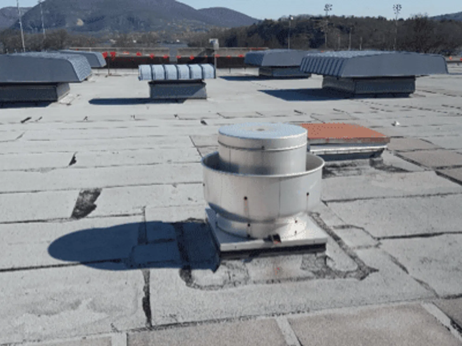 Flat commercial rooftop with ventilation fans and ducts under a clear sky and distant mountains.