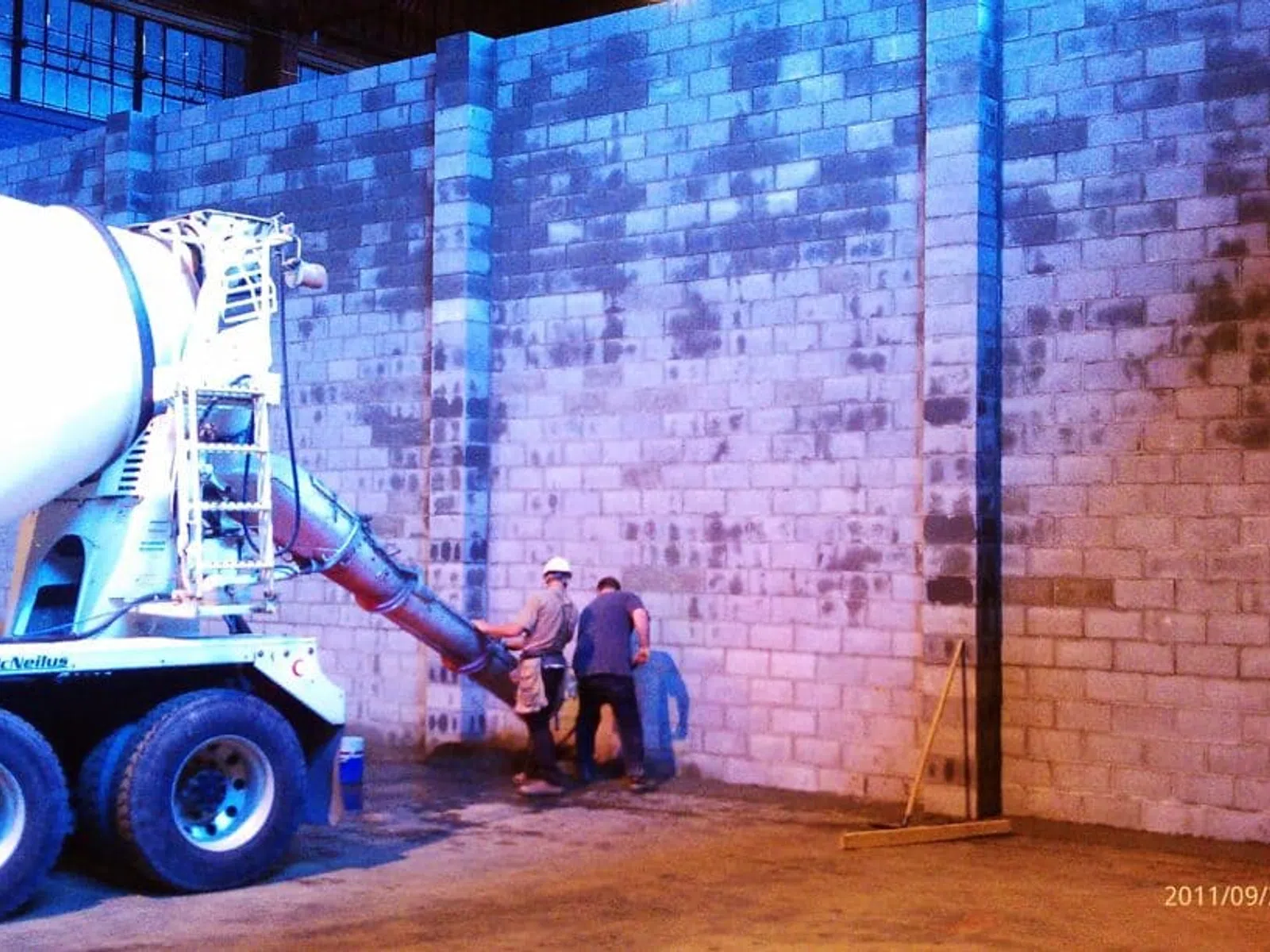Concrete mixer truck pouring concrete inside an industrial building under construction with workers.