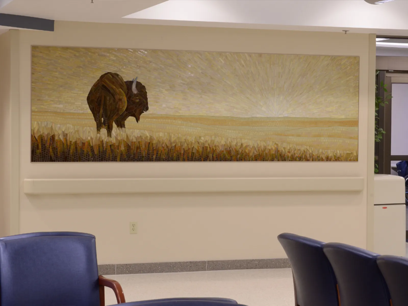 Large mural of a buffalo standing in a wheat field with a sunrise in the background in a modern waiting area.