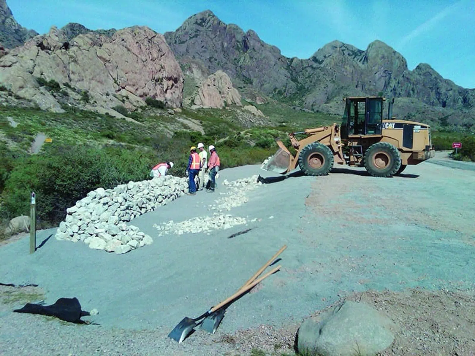 Construction workers and a bulldozer stacking rocks on a gravel slope with mountains in the background