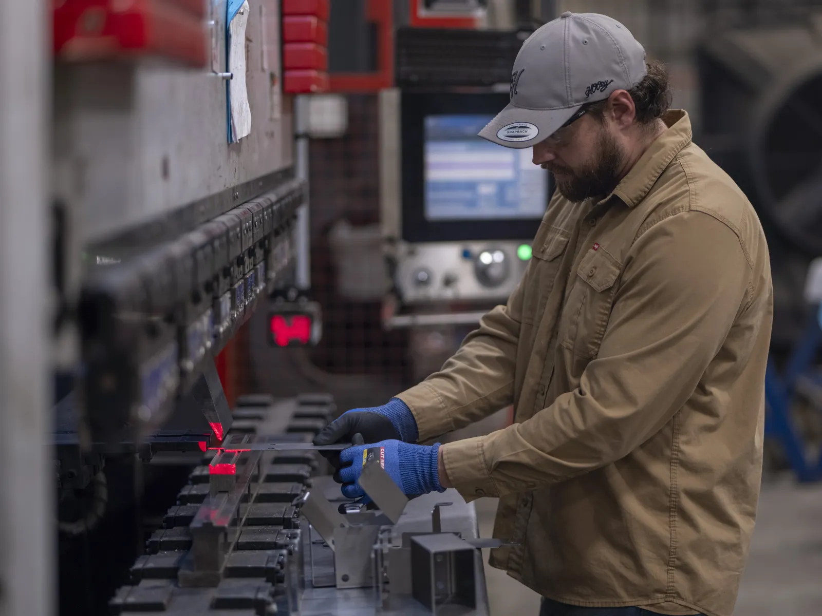 Worker in protective gloves operating industrial machinery in a manufacturing or metalworking facility.