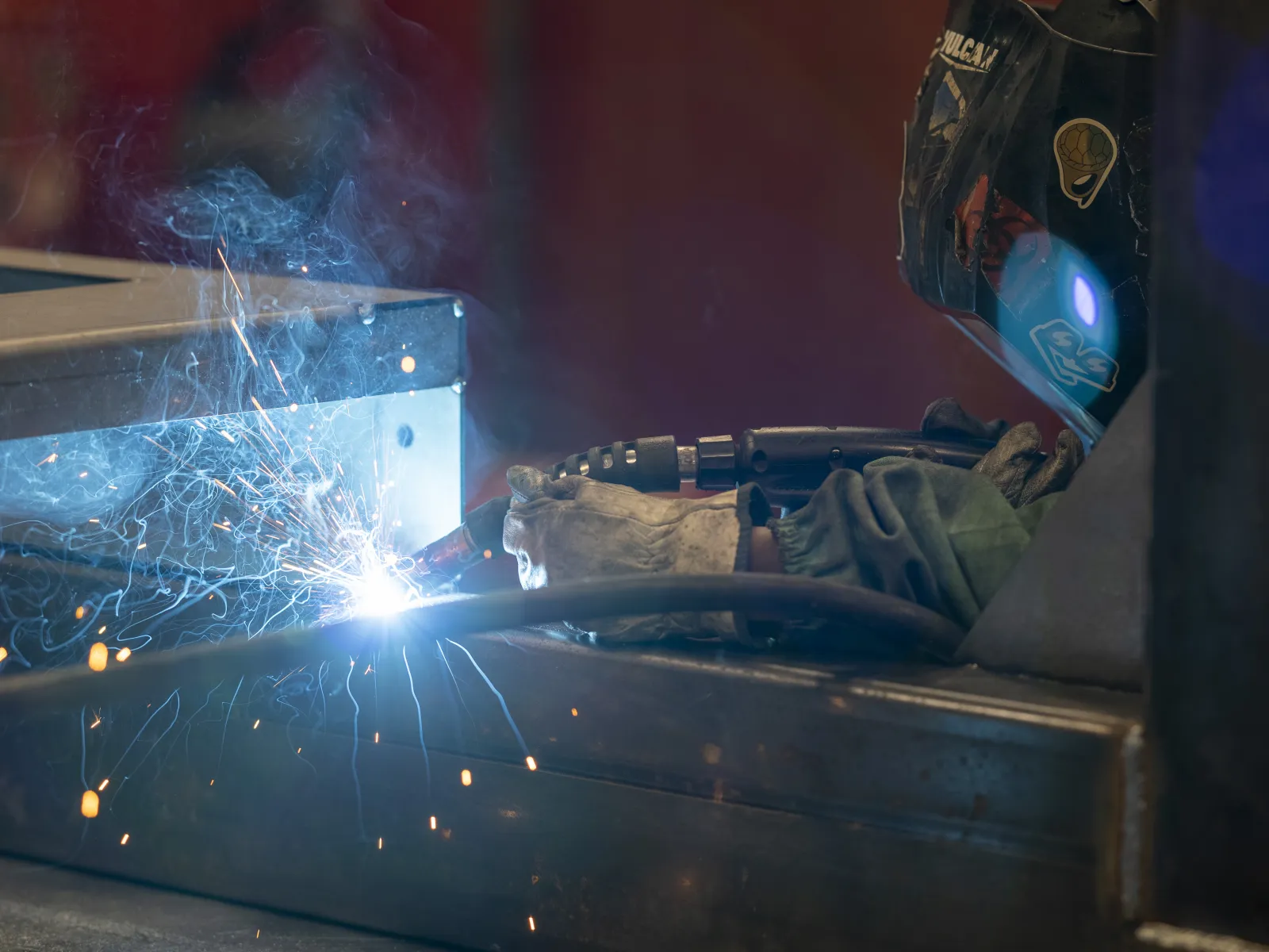 Welder in protective gear working with sparks and smoke welding metal components in industrial setting