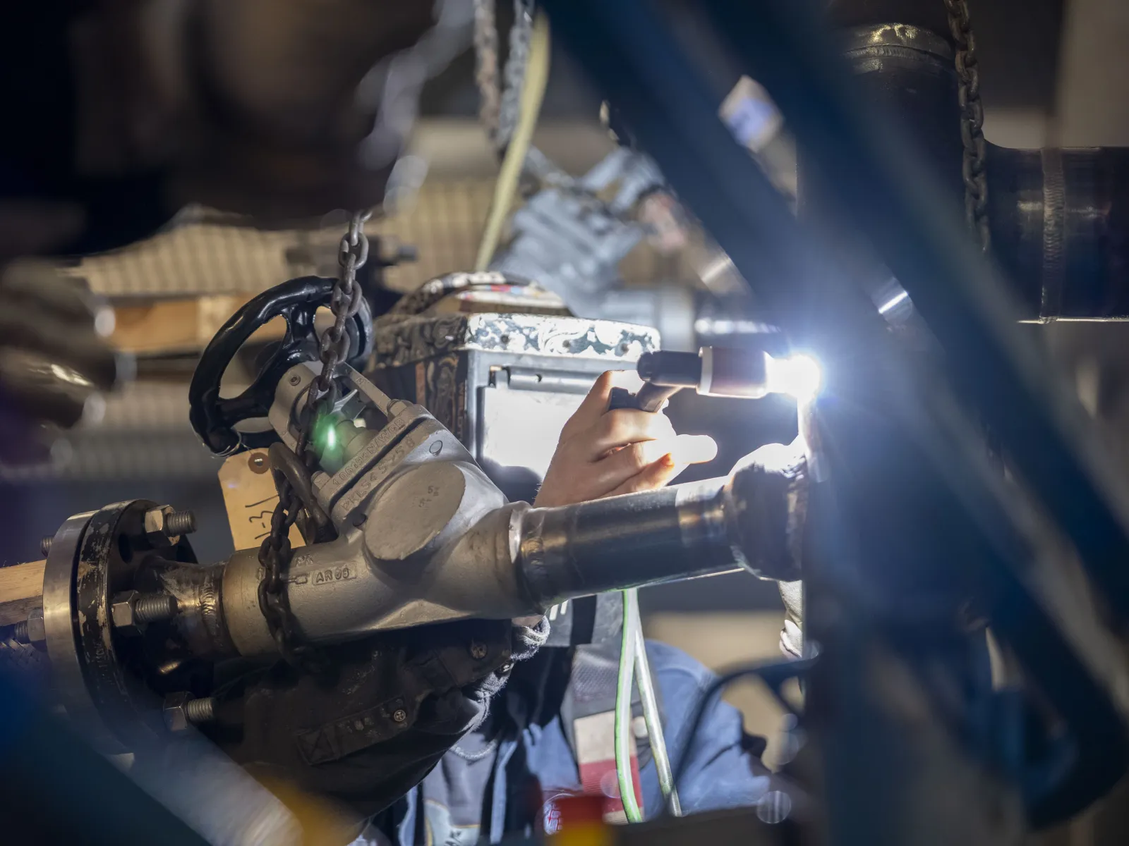 Welder fixes a large industrial metal pipe with welding torch creating bright sparks in a workshop environment