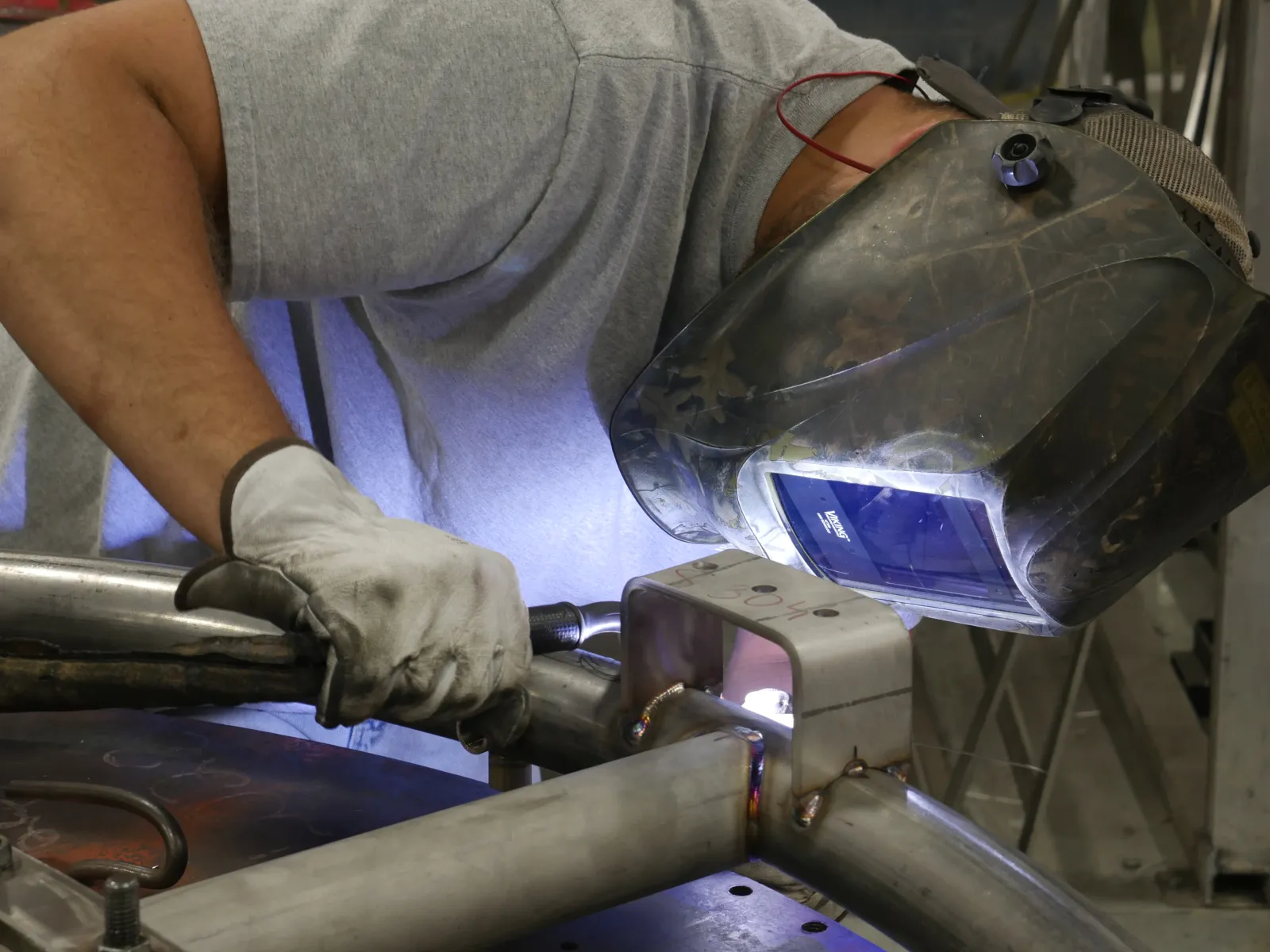Welder wearing protective helmet and gloves welding metal pipes in industrial workshop.