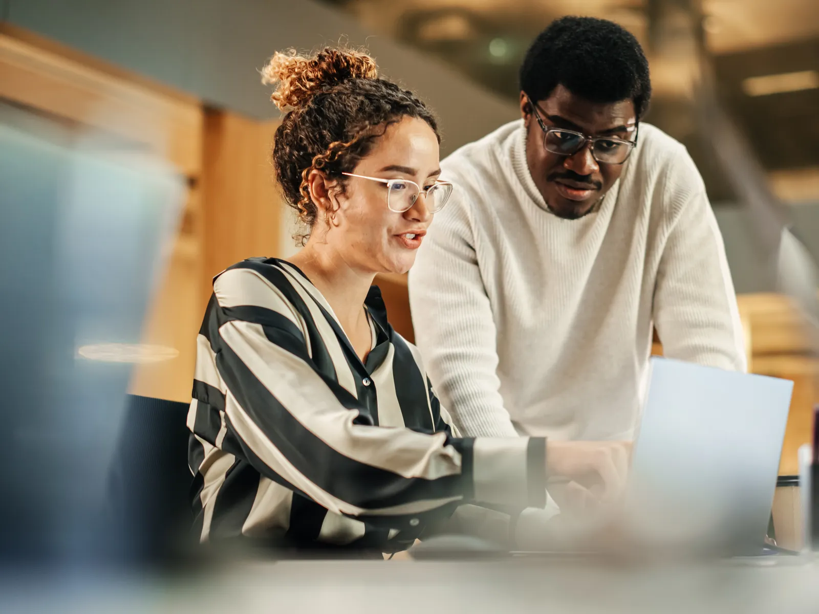 Two coworkers collaborate over a laptop in a modern office setting during daytime work hours