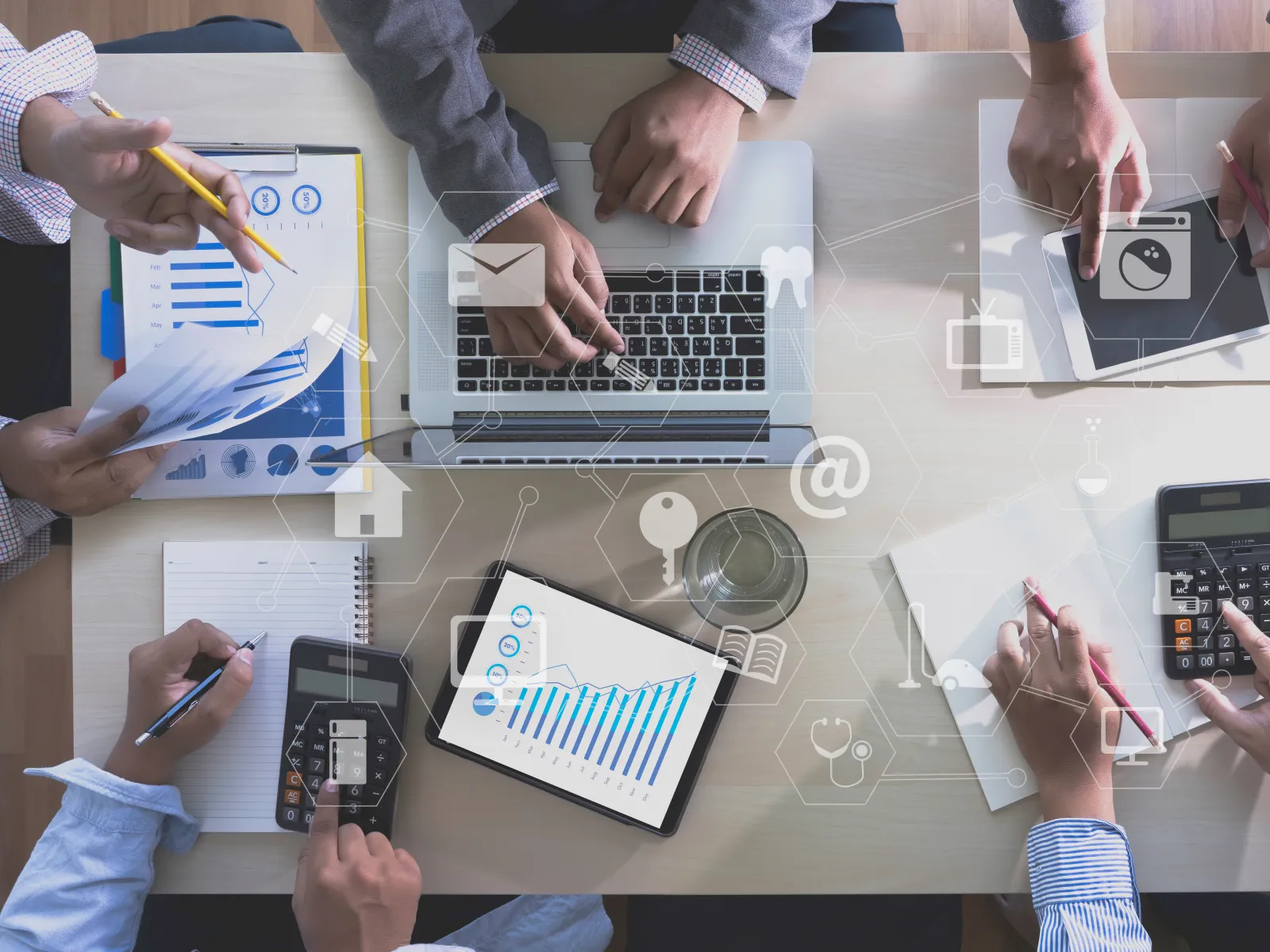 Business team analyzing charts and graphs using laptop, tablet, and calculators at shared desk workspace