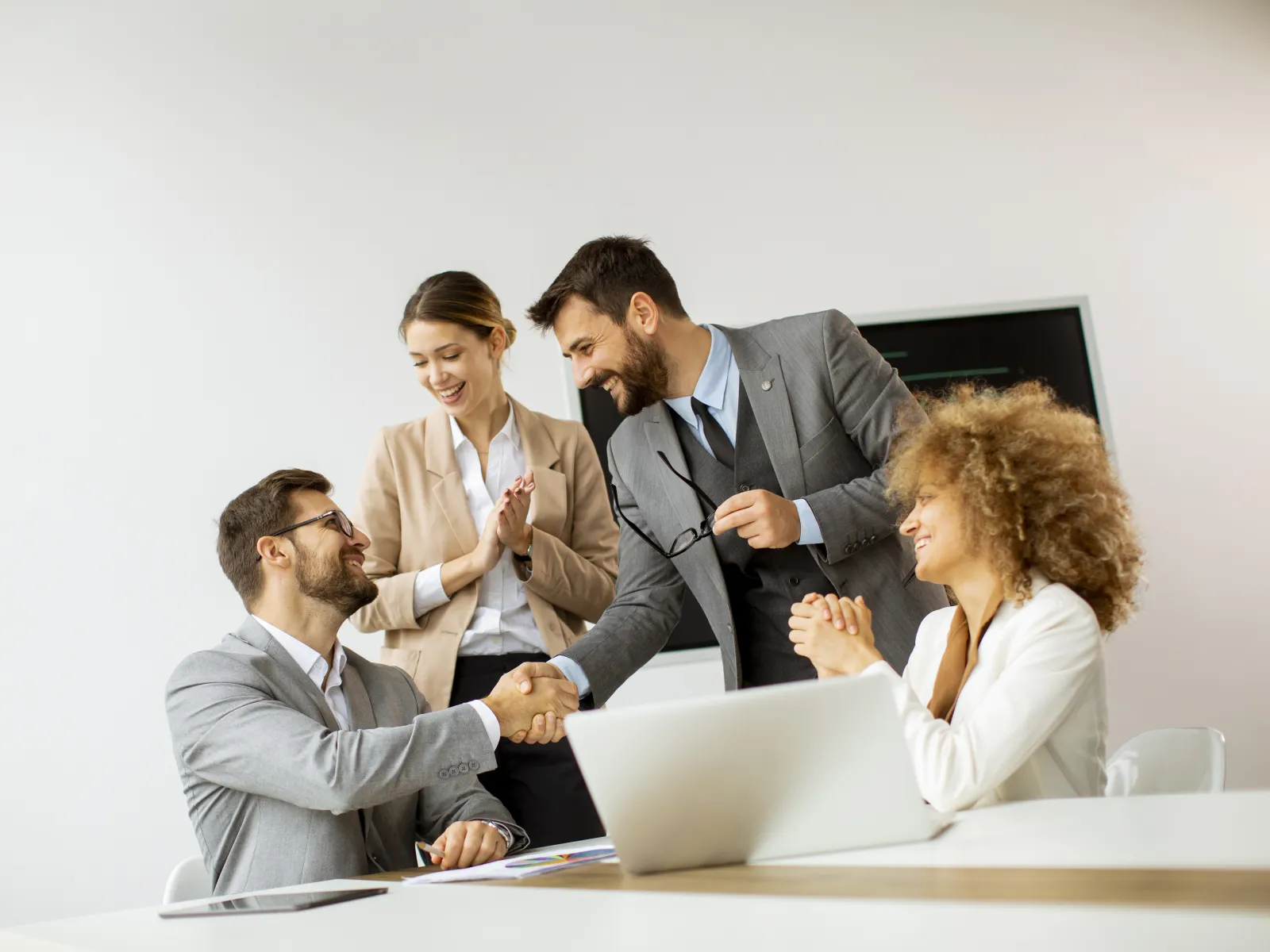 Business professionals shaking hands and celebrating successful meeting in a modern office with laptop.