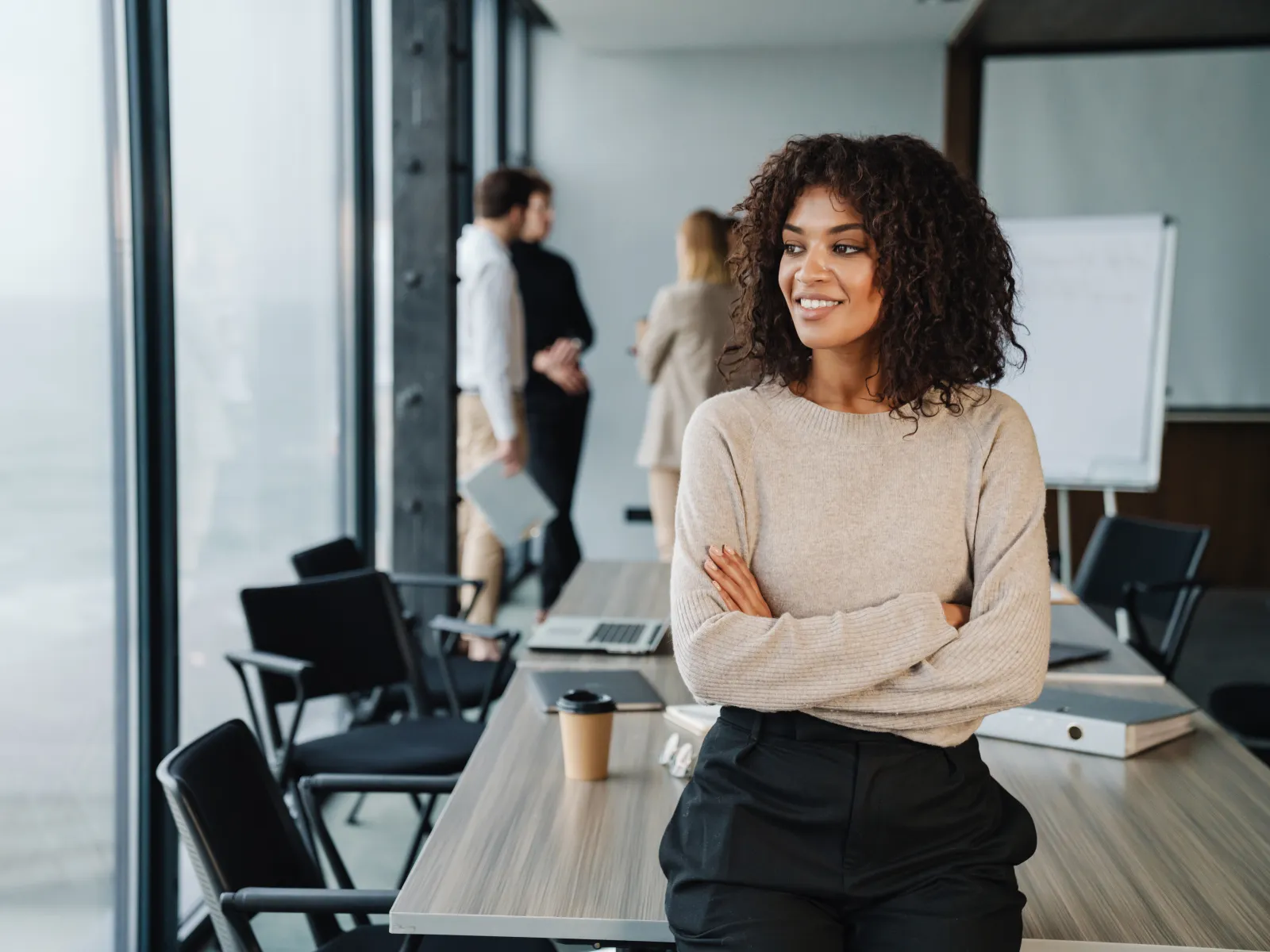 Confident businesswoman with curly hair standing by a conference table in a modern office space