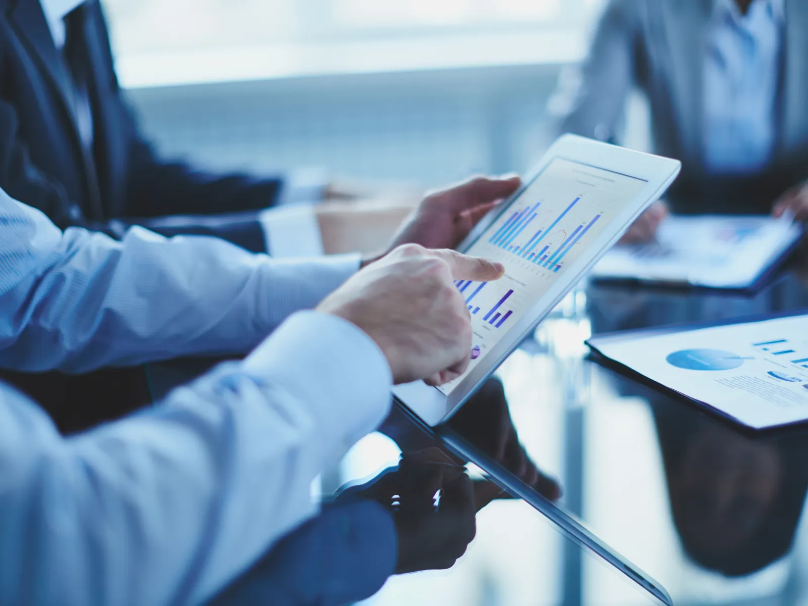 Business professionals reviewing charts and graphs on tablet during a meeting with printed reports on table