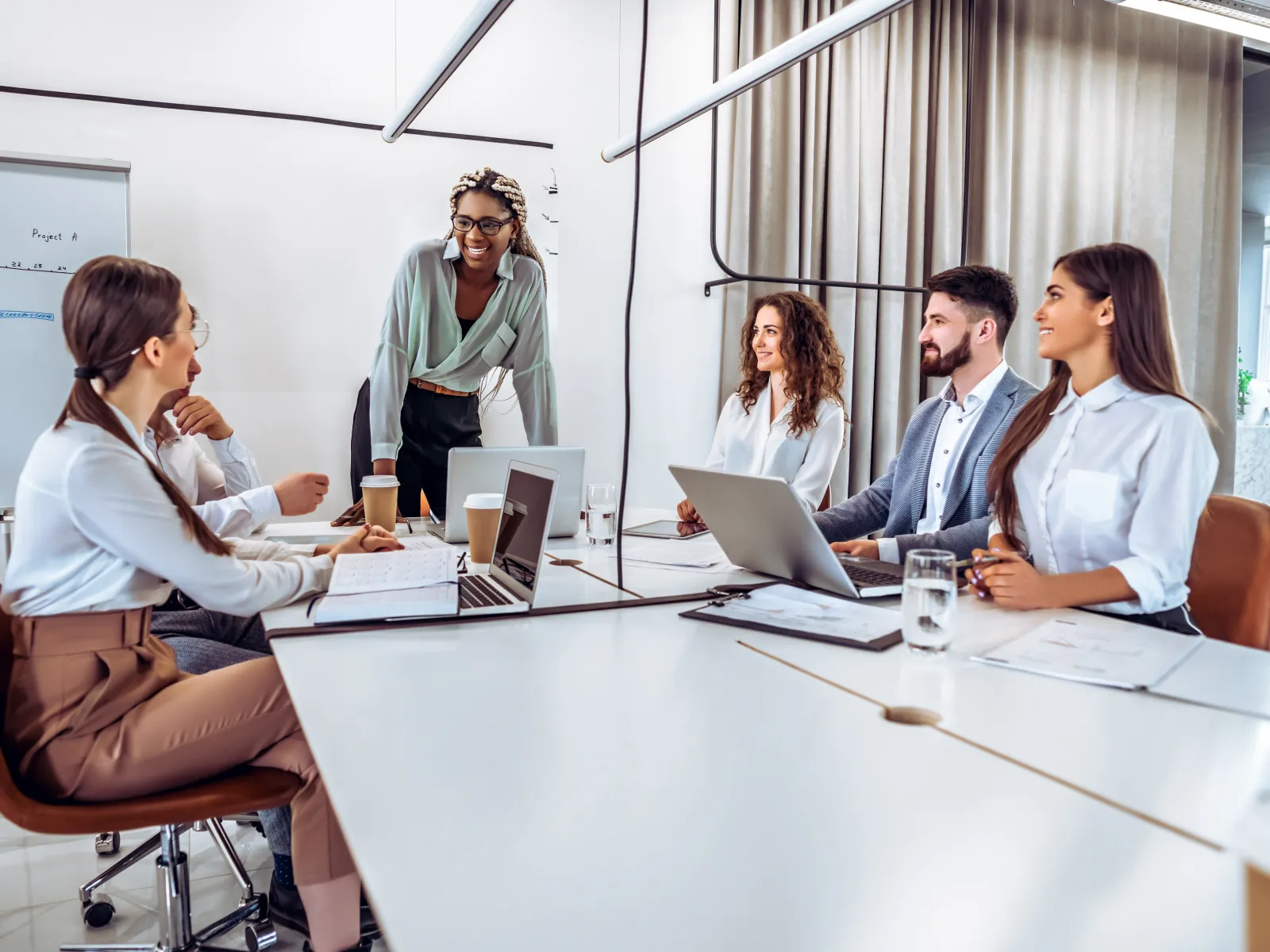 Diverse group of professionals collaborating in a modern office meeting with laptops and documents.