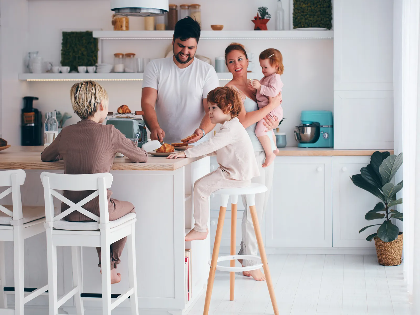 Family with two children enjoying breakfast together in bright, modern white kitchen with natural light.