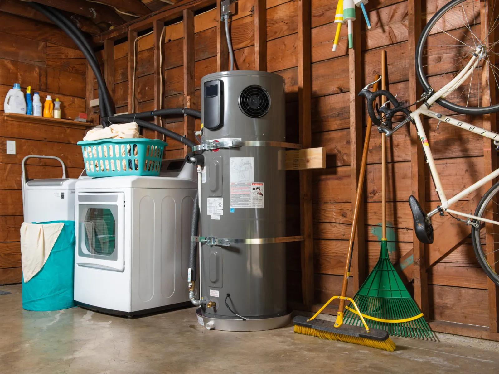 A functional garage with a water heater, washer, storage basket, and cleaning tools neatly arranged.