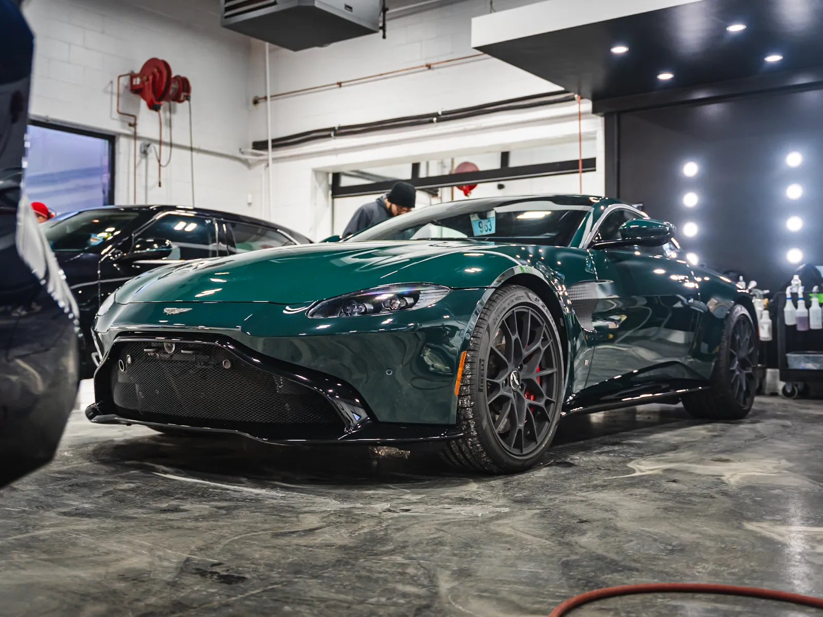 Dark green Aston Martin sports car parked indoors with shiny polished floor and bright studio lights.