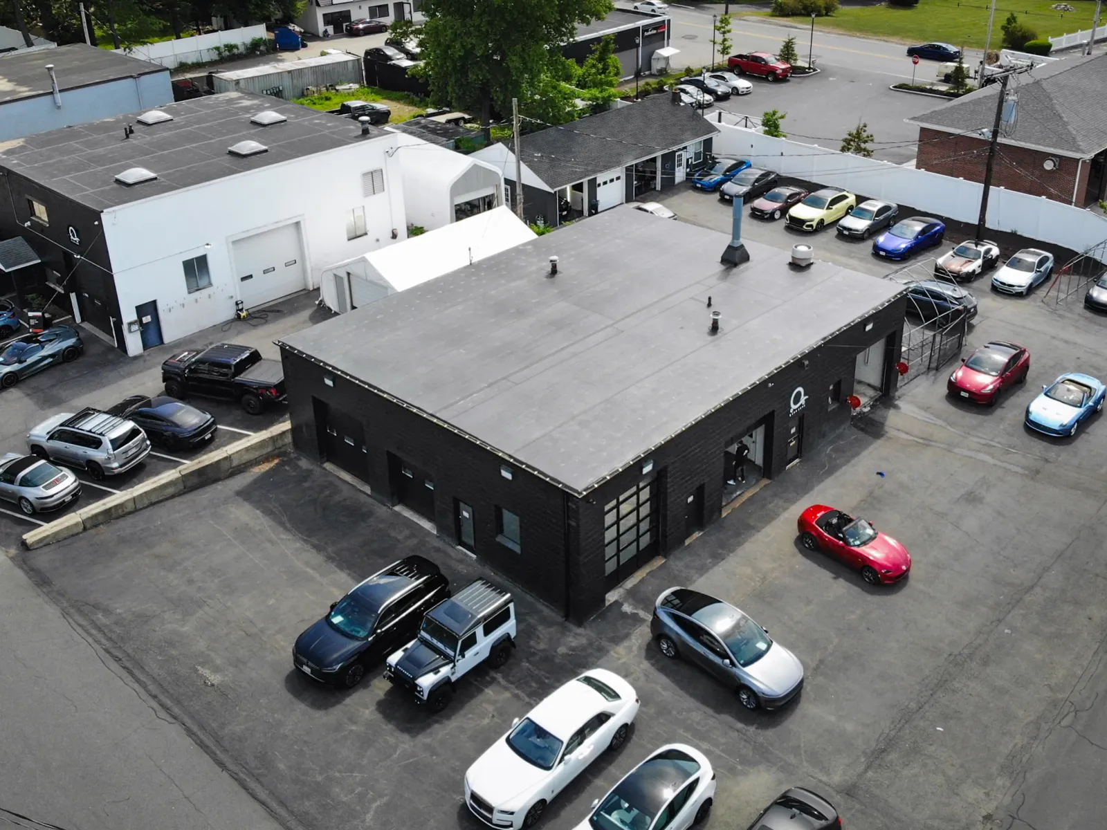 Aerial view of a black automotive shop with various parked cars around the building in a paved lot.