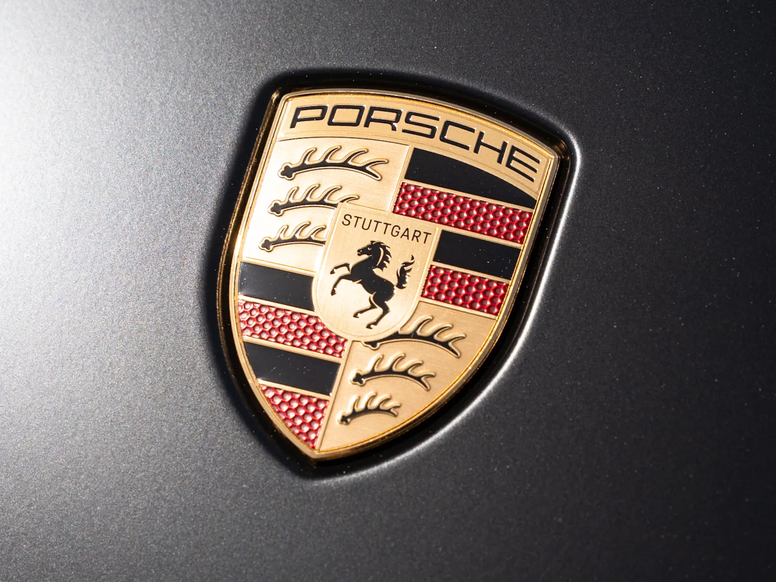 Close-up of the Porsche emblem on a dark metallic car surface showcasing its detailed design.