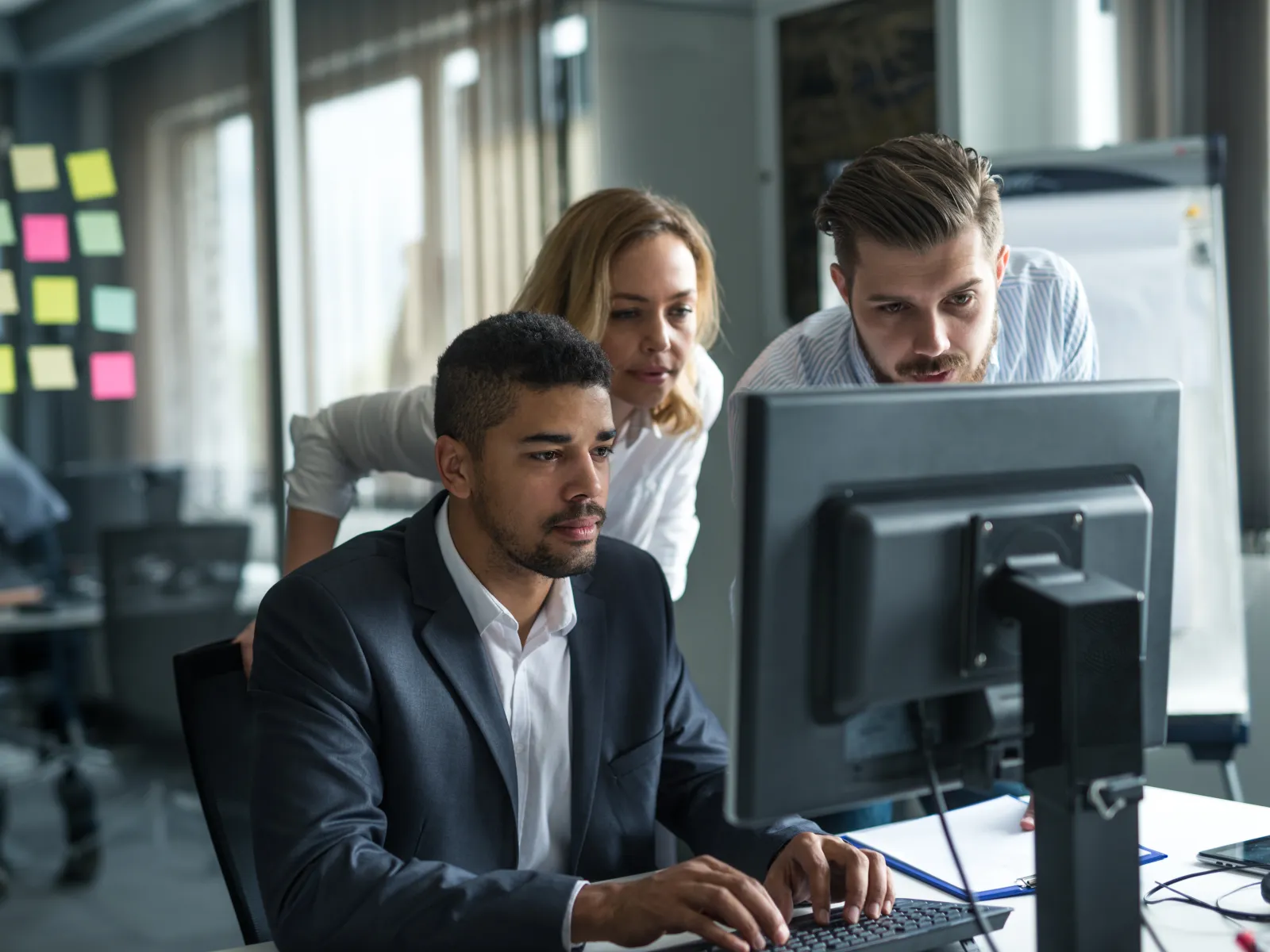 Three business colleagues collaborating and working on a desktop computer in a modern office setting.