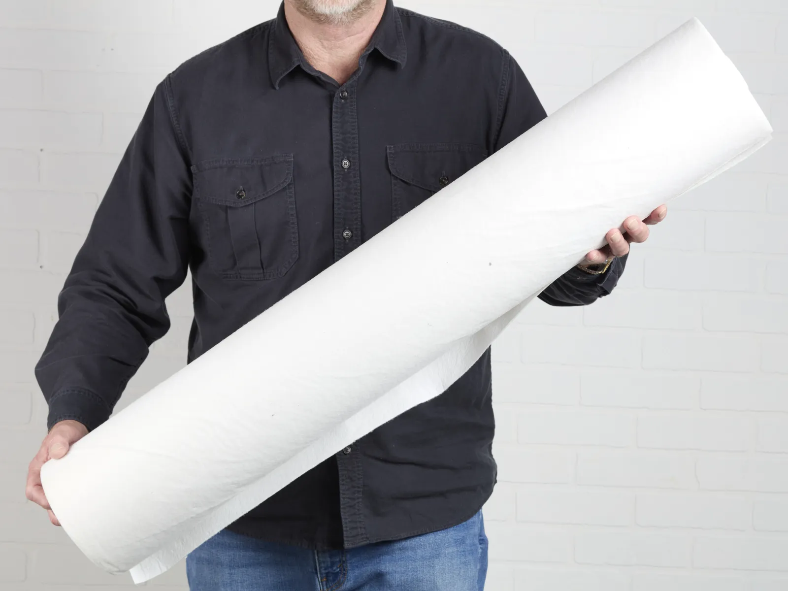 Man in black shirt holding a large rolled sheet of white paper against a white brick wall background