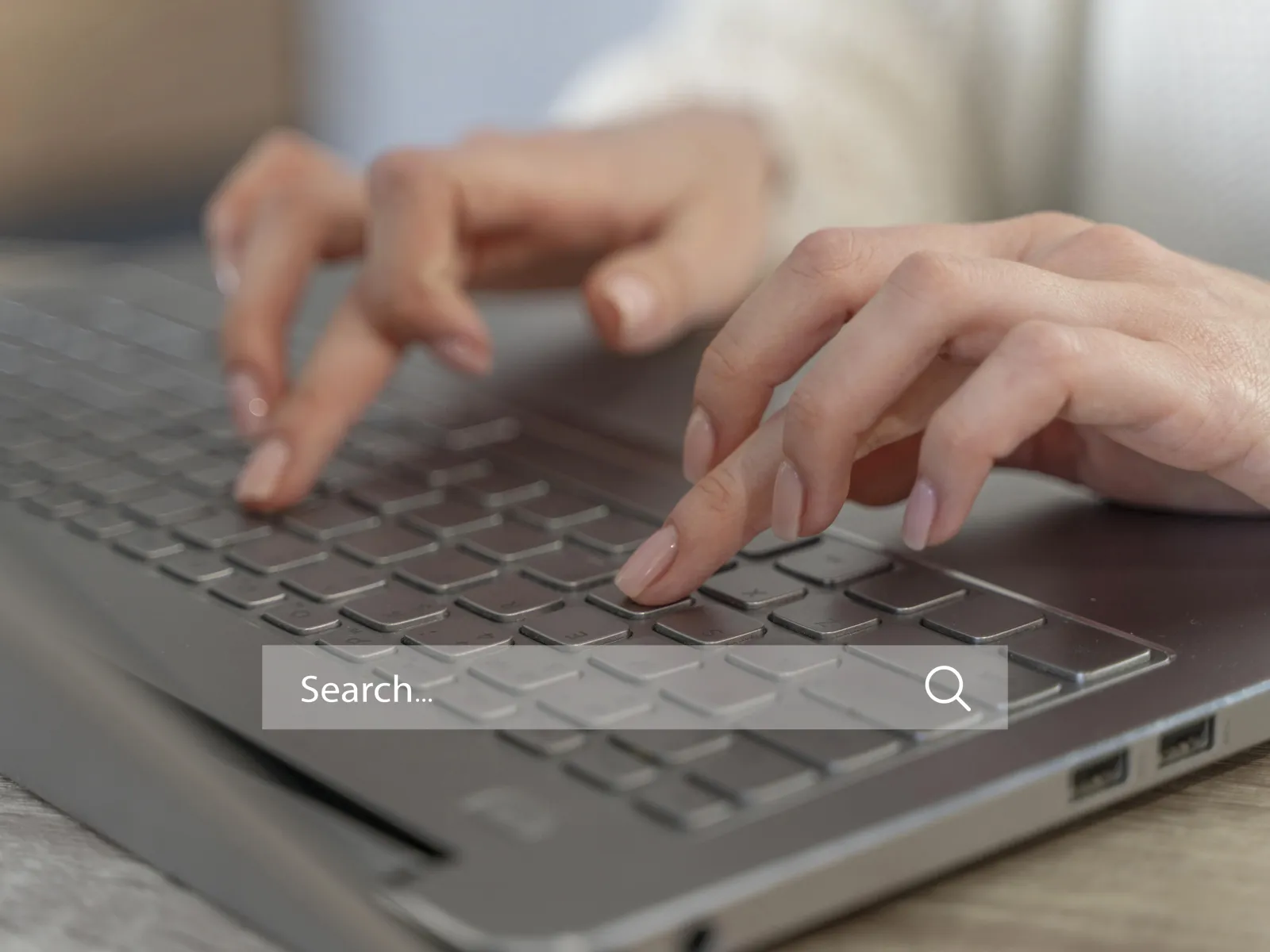 Close-up of hands typing on a laptop keyboard with a search bar visible.